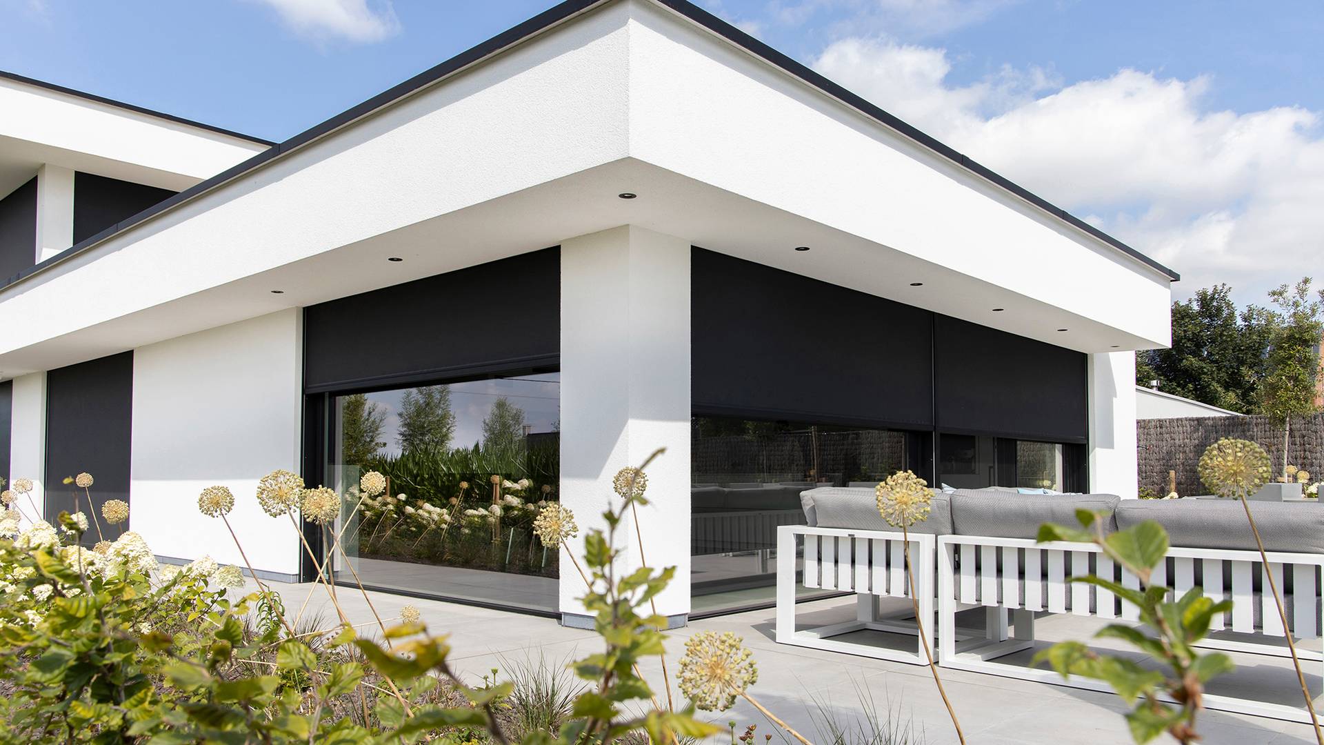 Modern home with aluminium ZIP‑screens installed over large windows, providing full exterior sun protection above a terrace with outdoor seating.