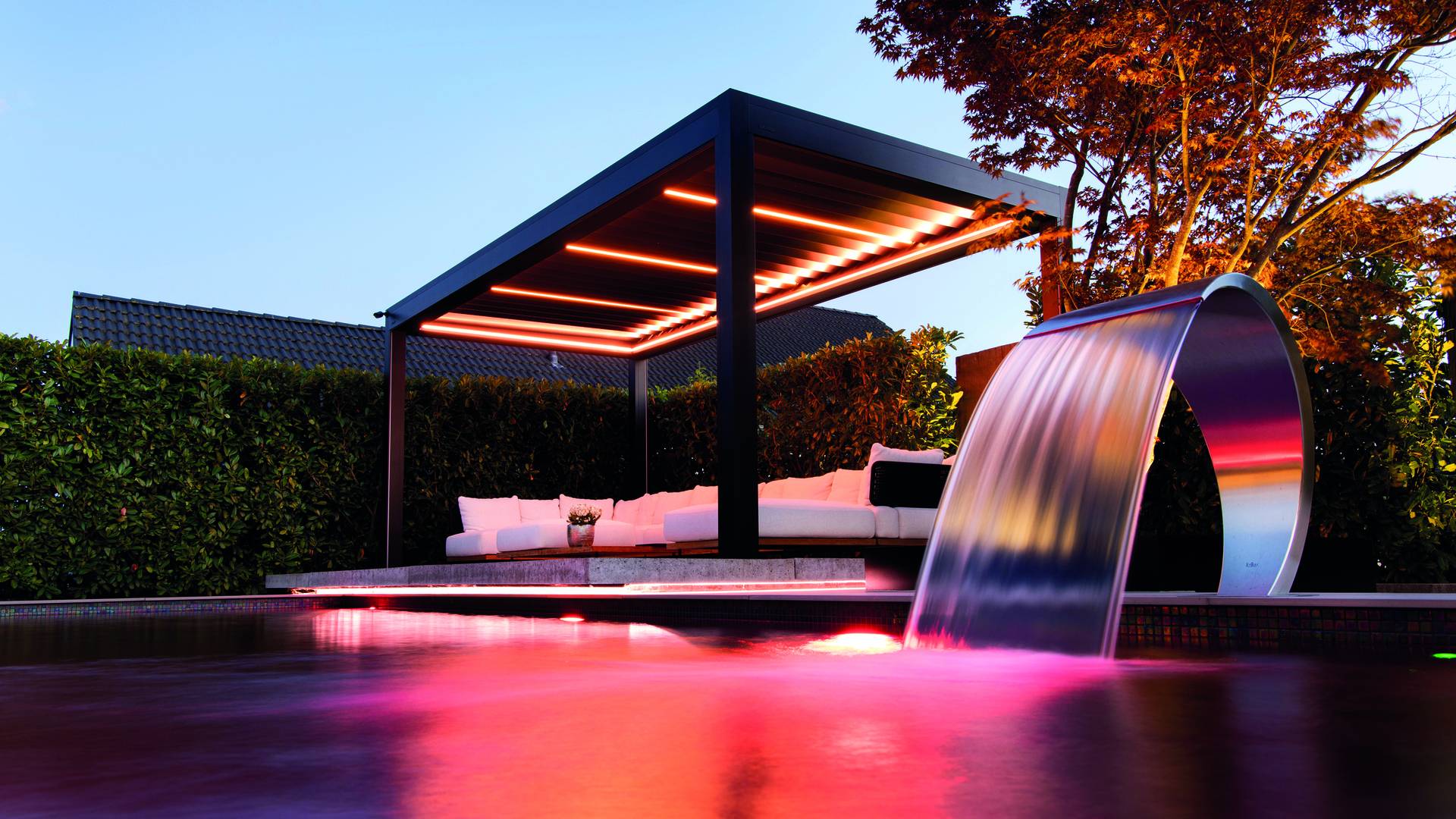 Pergola in alluminio con tetto a lamelle aperte che crea ombre a strisce su una lounge esterna, con una persona che pratica yoga sulla terrazza della piscina.