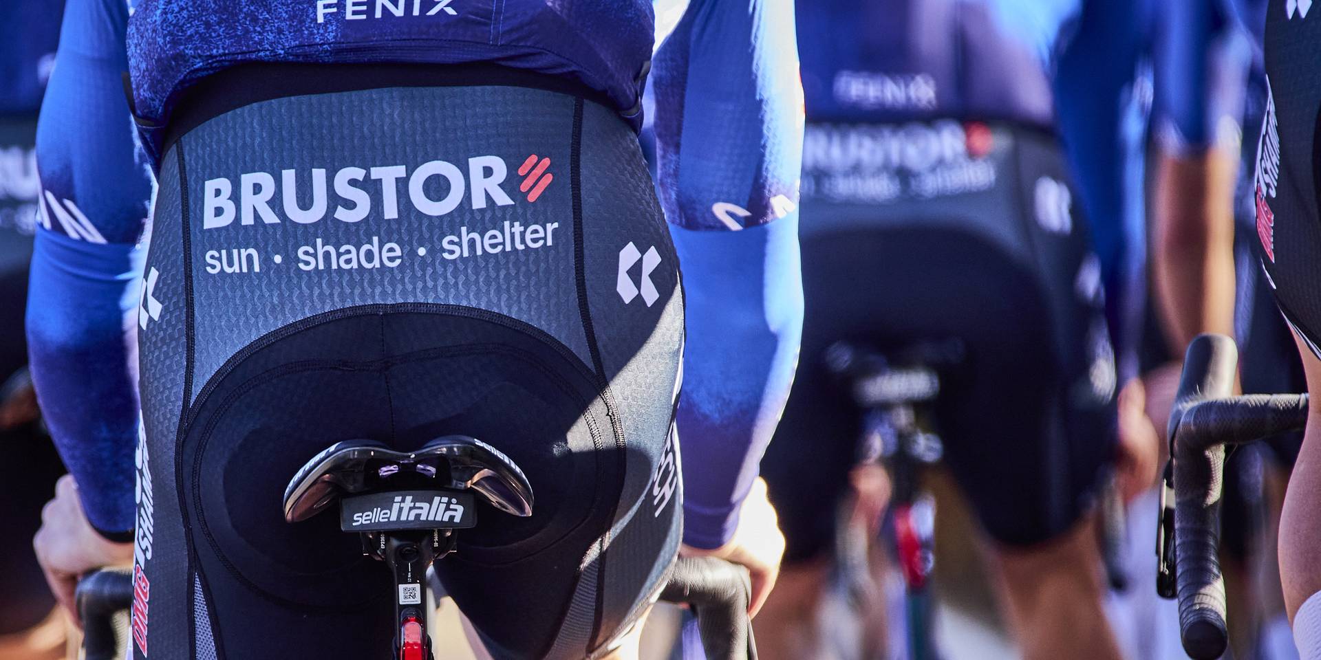 Close‑up van de Alpecin–Premier Tech‑teamkledij met het Brustor Sun • Shade • Shelter‑logo op de koersbroeken.