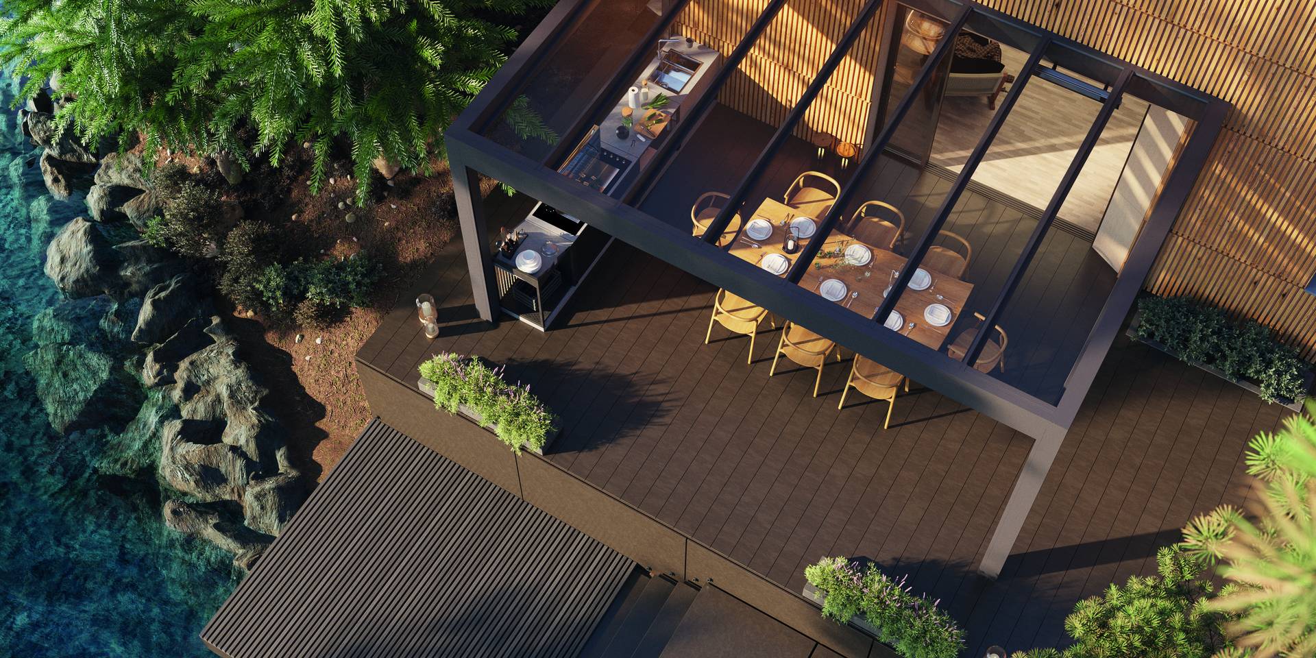 Vue aérienne d’une pergola en aluminium à toiture fixe couvrant un espace repas extérieur avec cuisine intégrée, installée sur une terrasse près d’une maison à façade en bois et d’un point d’eau.