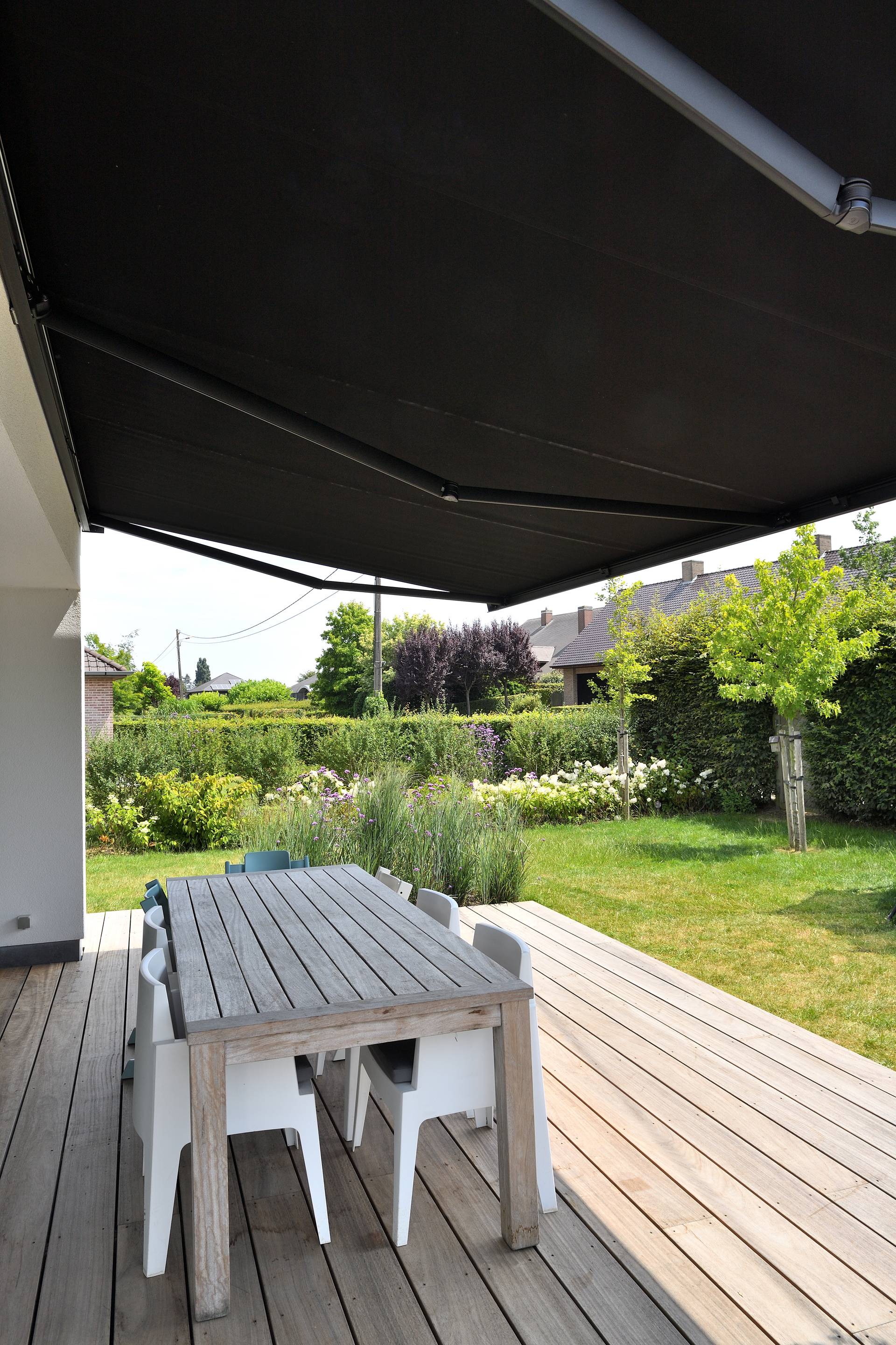 Store banne rétractable en aluminium ombrageant une terrasse en bois avec table de repas extérieure, donnant sur un jardin paysager.