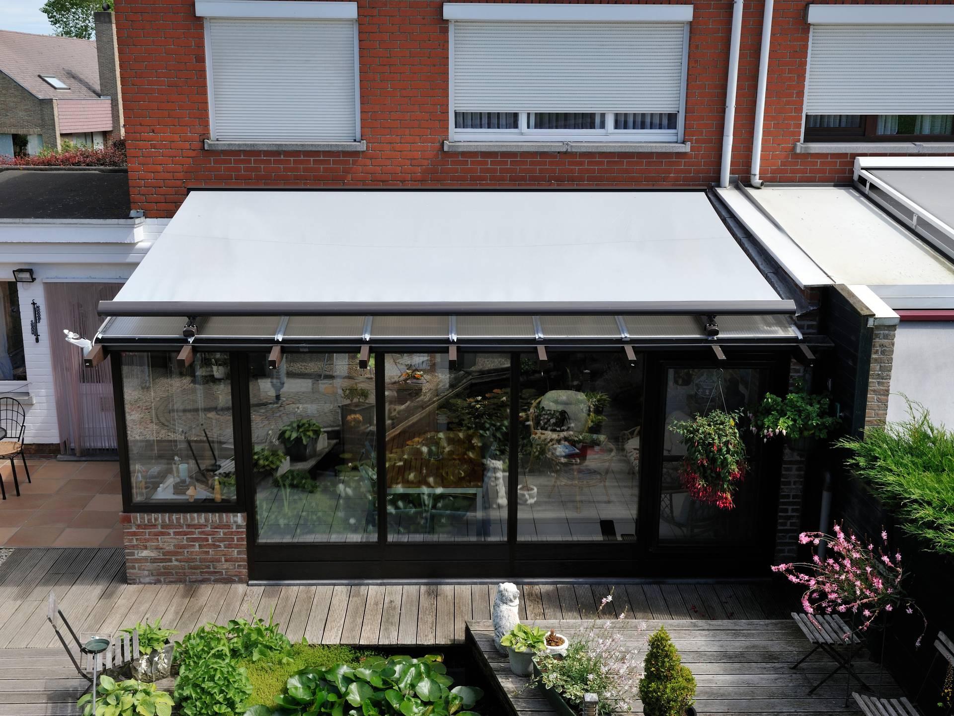 Brustor B127 conservatory awning mounted above an angled glass veranda roof providing exterior sun protection on a modern brick home