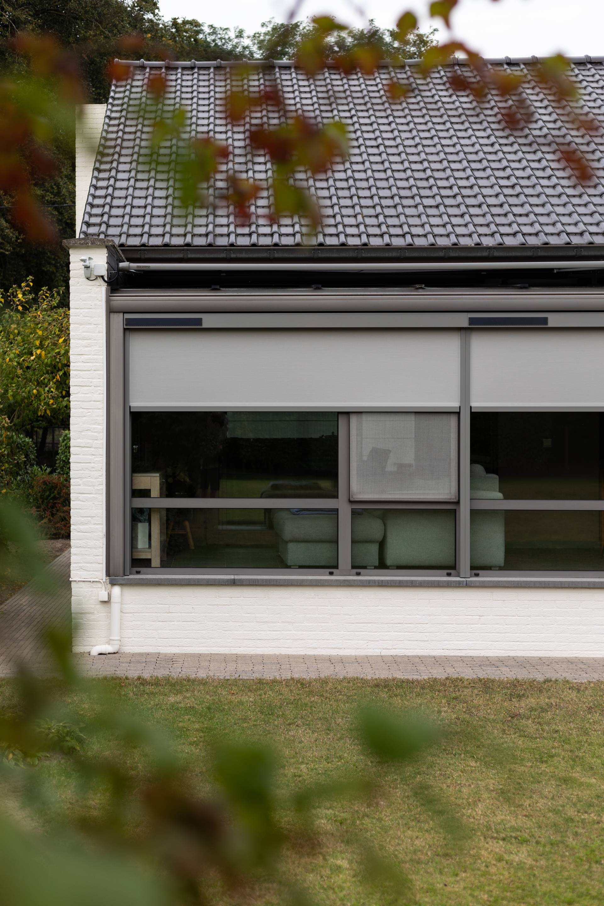 Woninguitbouw met aluminium ZIP‑screens voor grote ramen, die buitenzonwering bieden met uitzicht op de tuin.