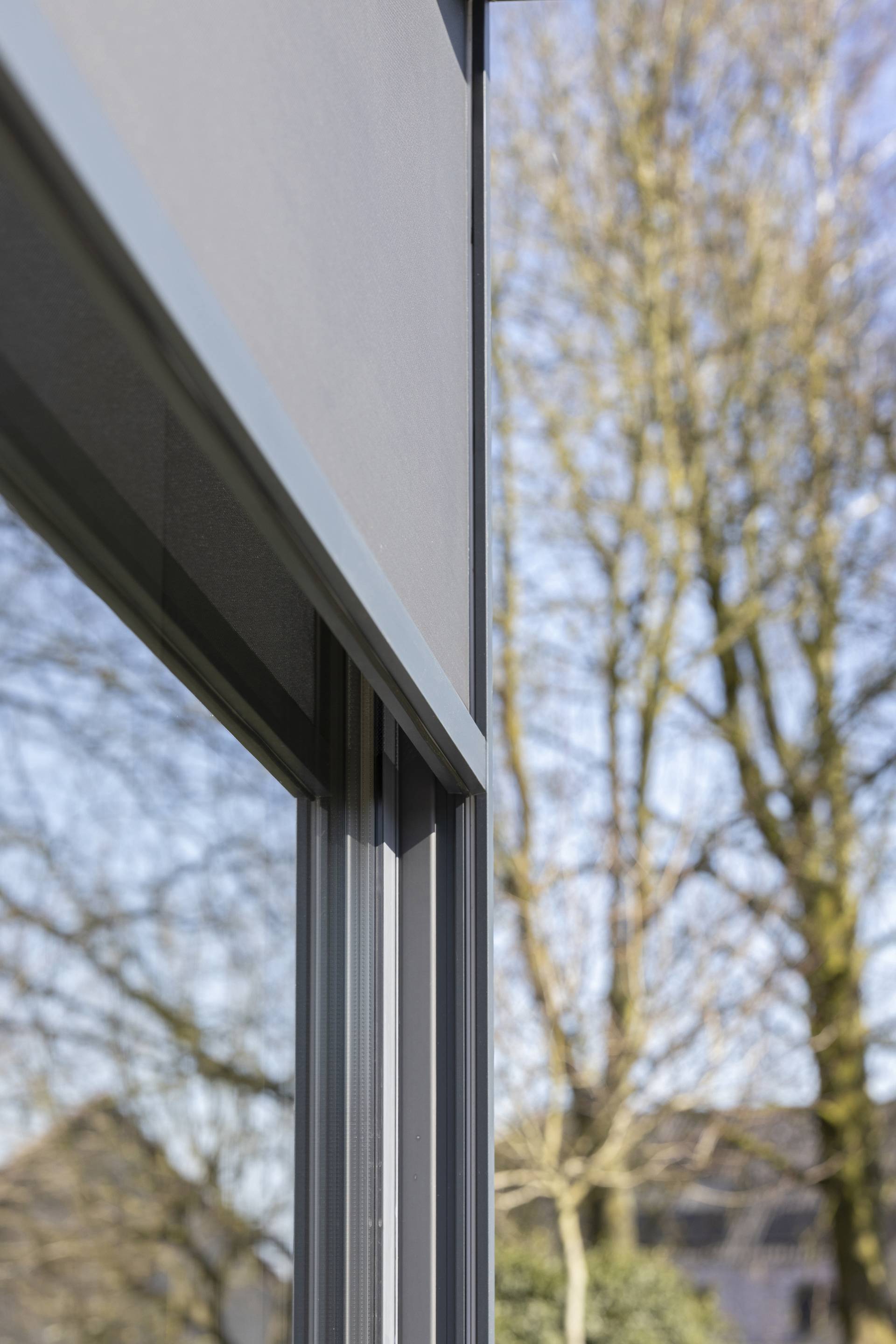Close‑up van een aluminium ZIP‑screen met zijgeleiders, gemonteerd op een buitenraamkader.