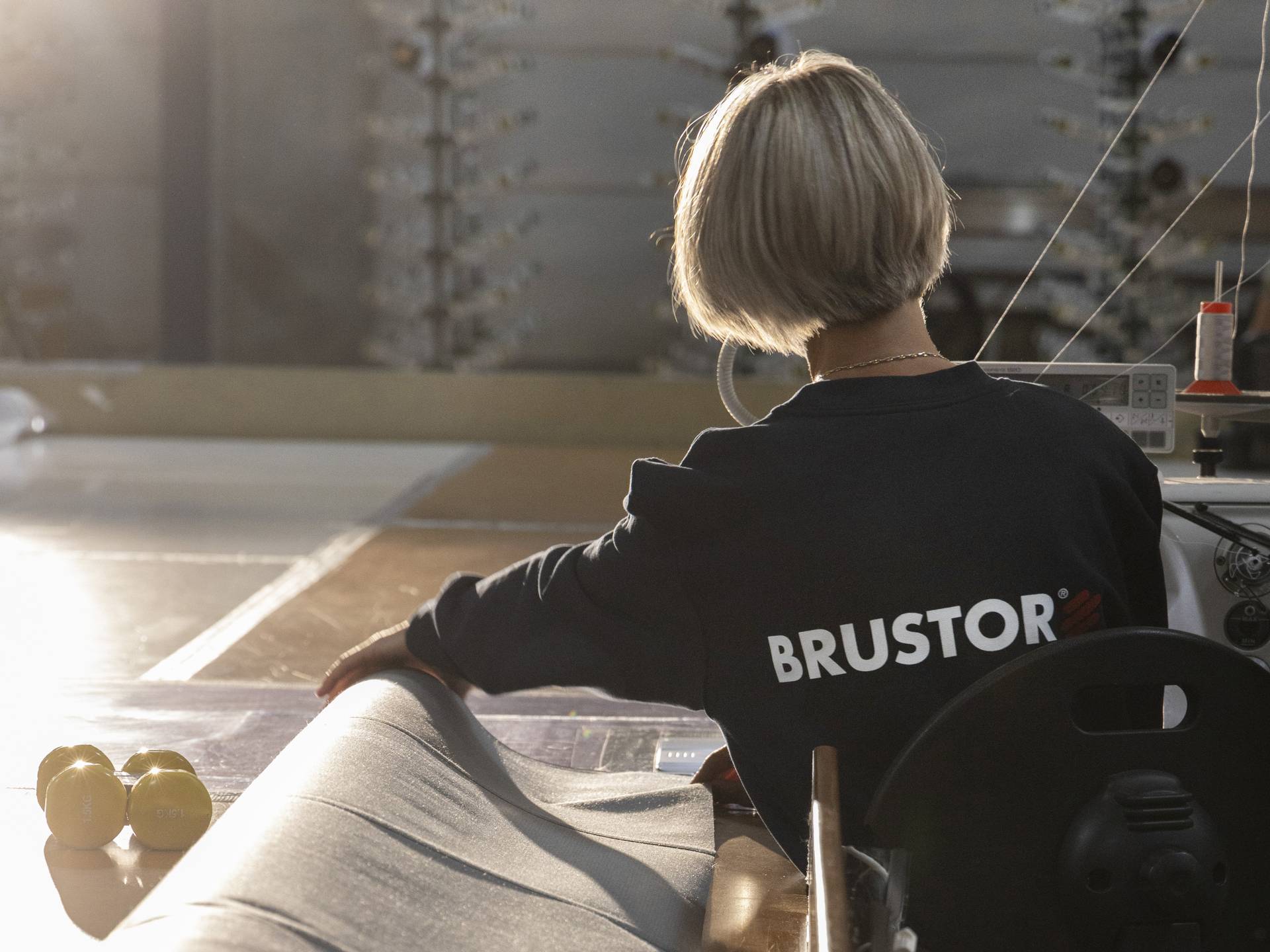 Medewerker die stof controleert op een productietafel in een werkplaats, met zichtbaar BRUSTOR-logo op de kleding.