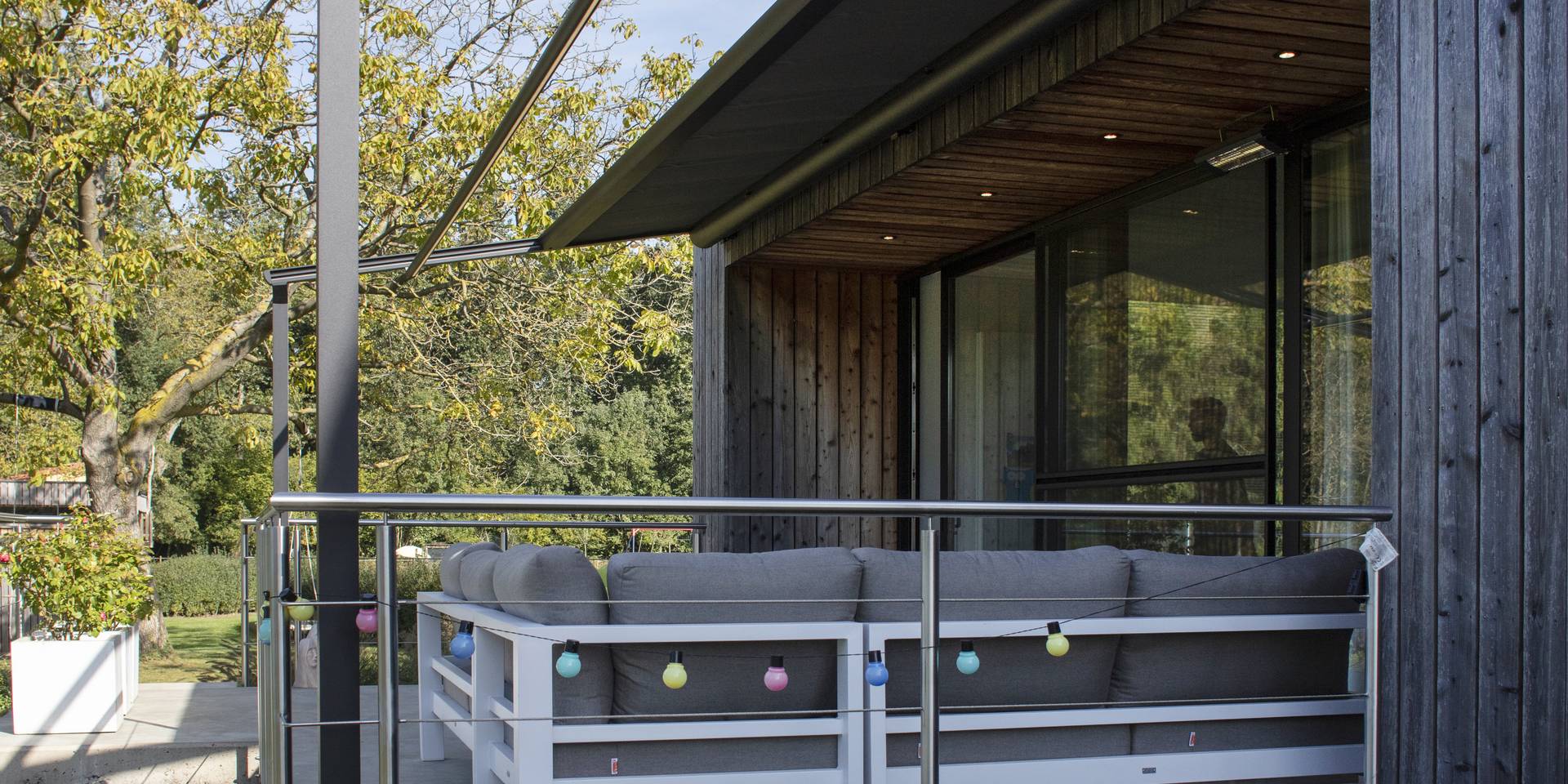 Store banne rétractable déployé au‑dessus d’une terrasse surélevée avec espace lounge extérieur, fixé à une façade moderne en bois.