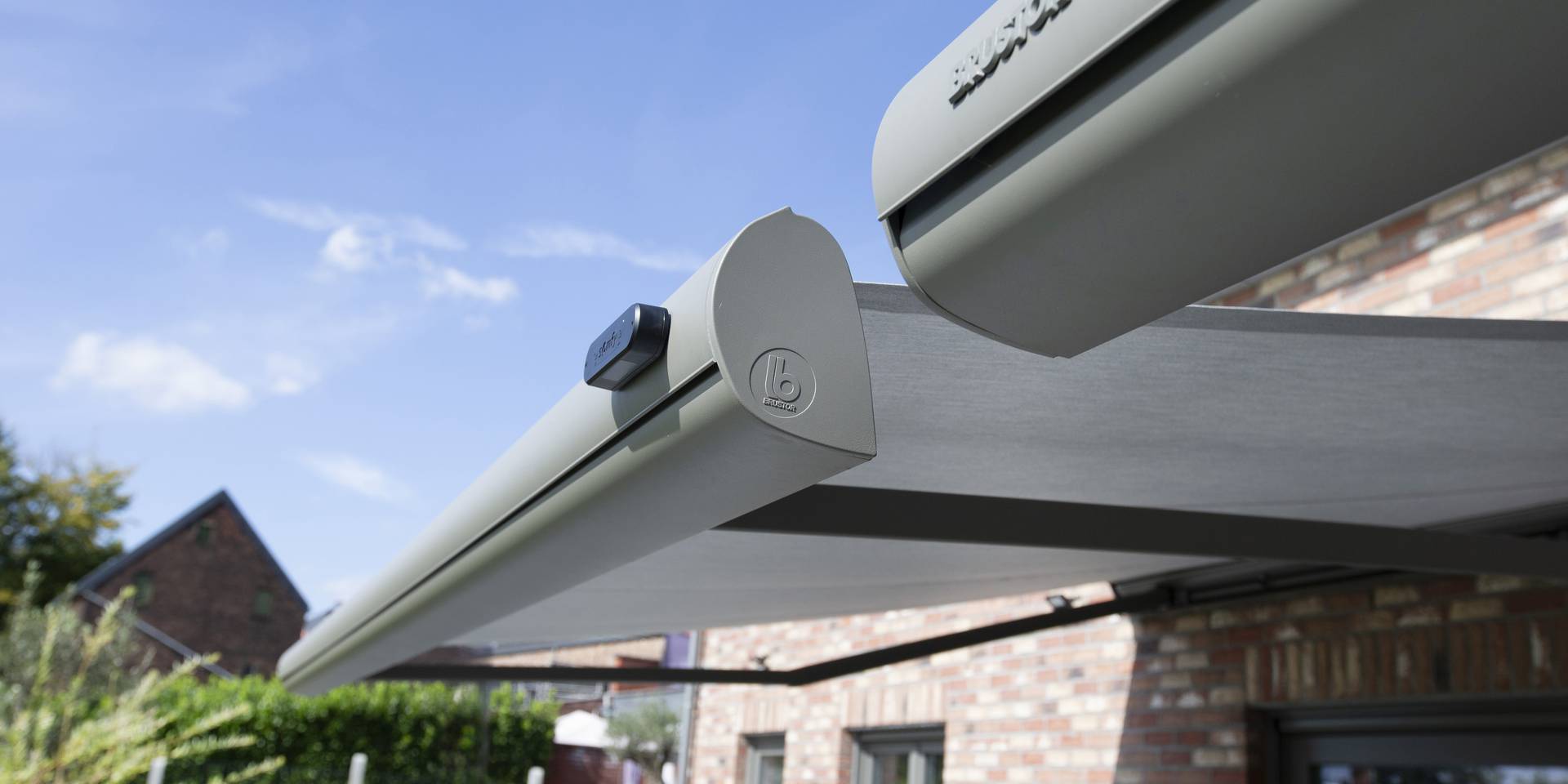 Gros plan sur un store banne rétractable montrant la cassette, le bras articulé et la toile déployée devant une façade en briques.