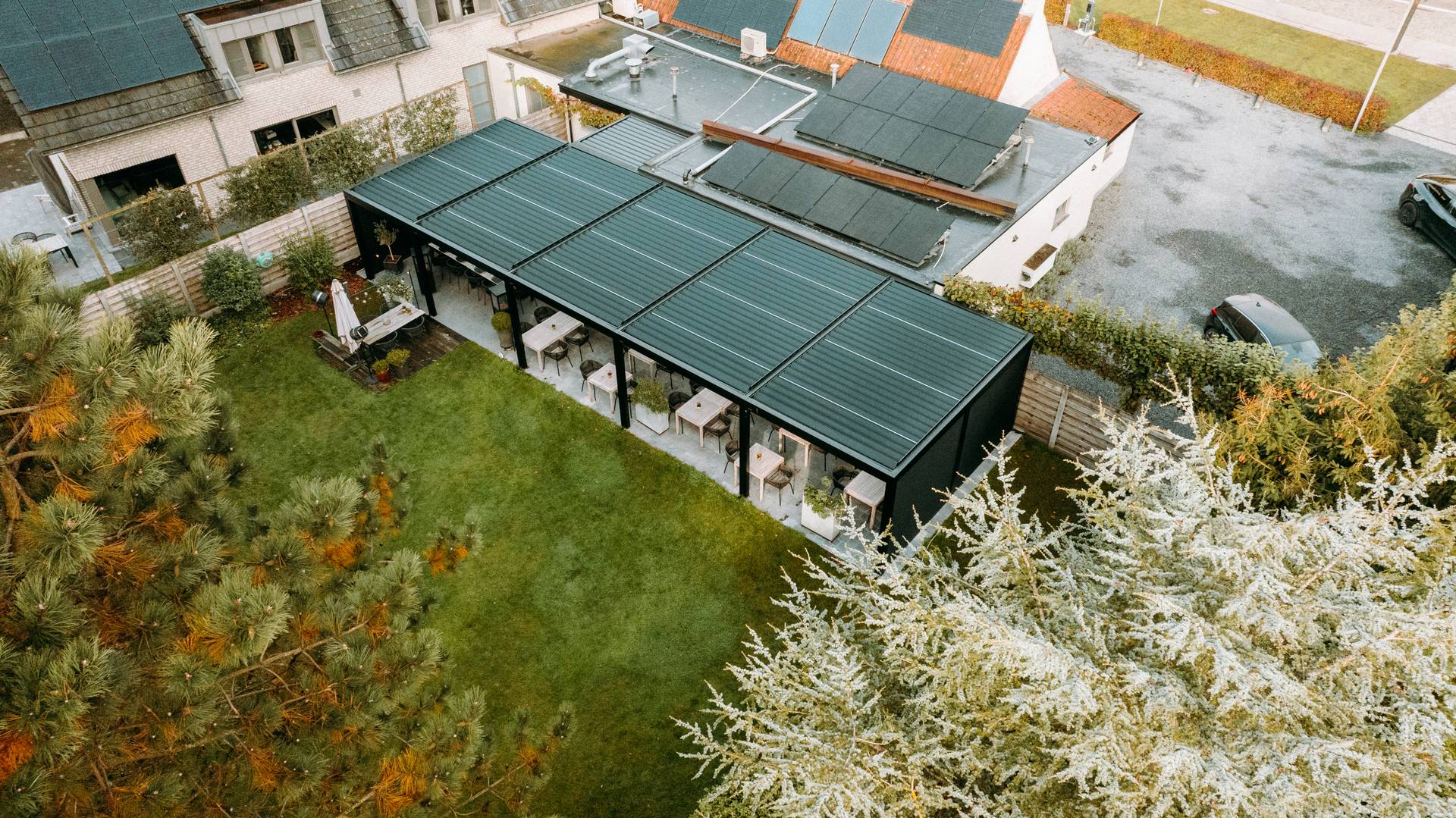 Vista aerea di un’installazione di pergola moderna che copre un’area pranzo esterna accanto a un giardino curato.