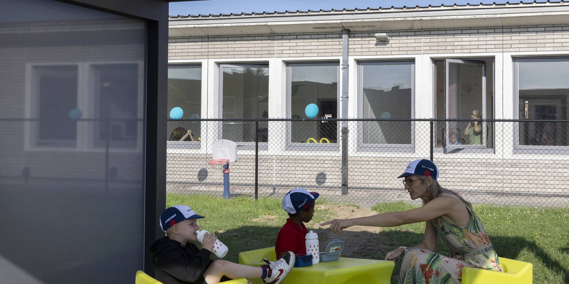 Aluminium-Pergola, die einen schattigen Außenbereich schafft, in dem Kinder mit einer Betreuungsperson an einem niedrigen Tisch auf dem Schulhof sitzen.