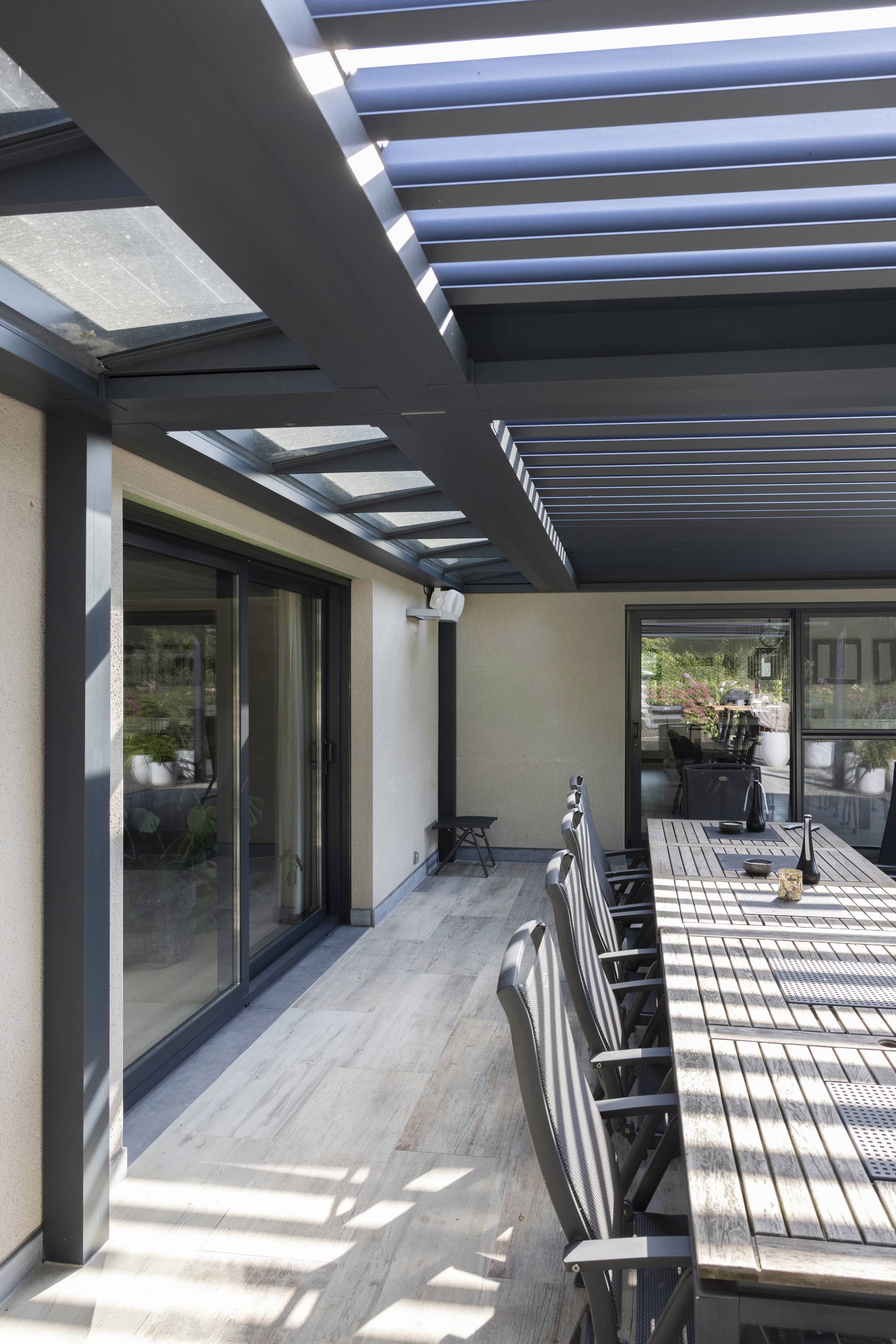 Aluminium‑Pergola B720 mit festem Glaselement und verstellbaren XL‑Lamellen über einem großzügigen Essbereich im Freien mit integrierter Heizstrahler