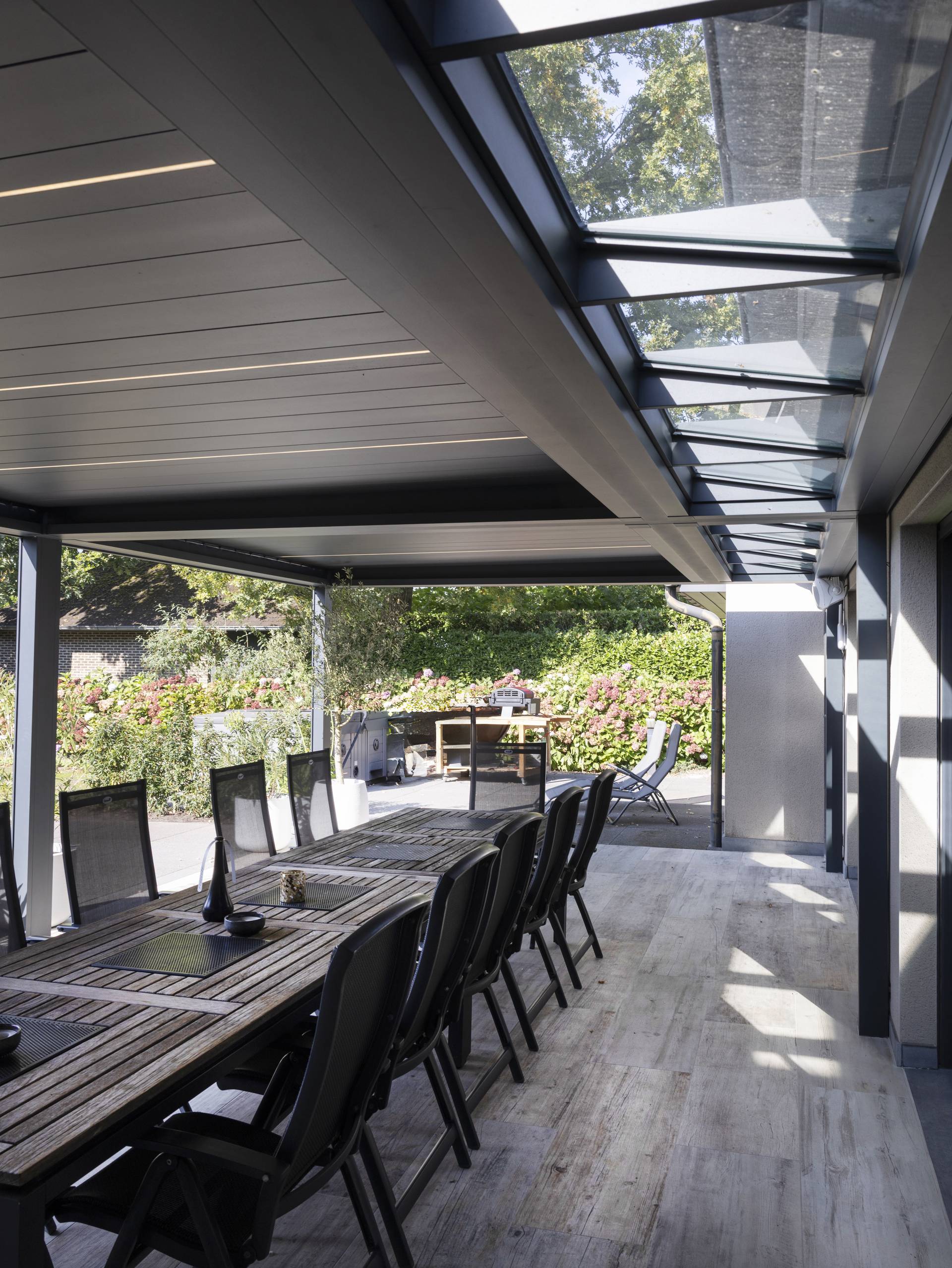 Aluminium‑Pergola B720 mit festem Glaselement und verstellbaren XL‑Lamellen über einem großzügigen Essbereich im Freien neben einem modernen Haus