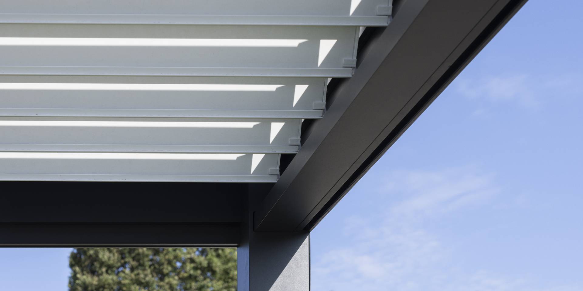 Nahaufnahme einer Aluminium-Pergola mit verstellbaren Lamellen vor blauem Himmel.