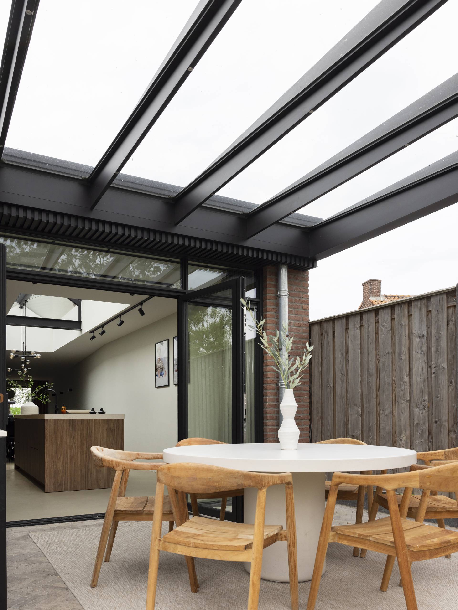 Pergola B800 en aluminium avec toit en verre attenante à la maison, couvrant un espace repas extérieur lumineux ouvert sur l’intérieur