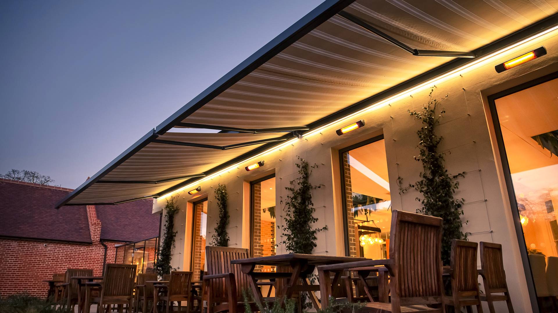 Pergola in alluminio con tetto a lamelle aperte che crea ombre a strisce su una lounge esterna, con una persona che pratica yoga sulla terrazza della piscina.