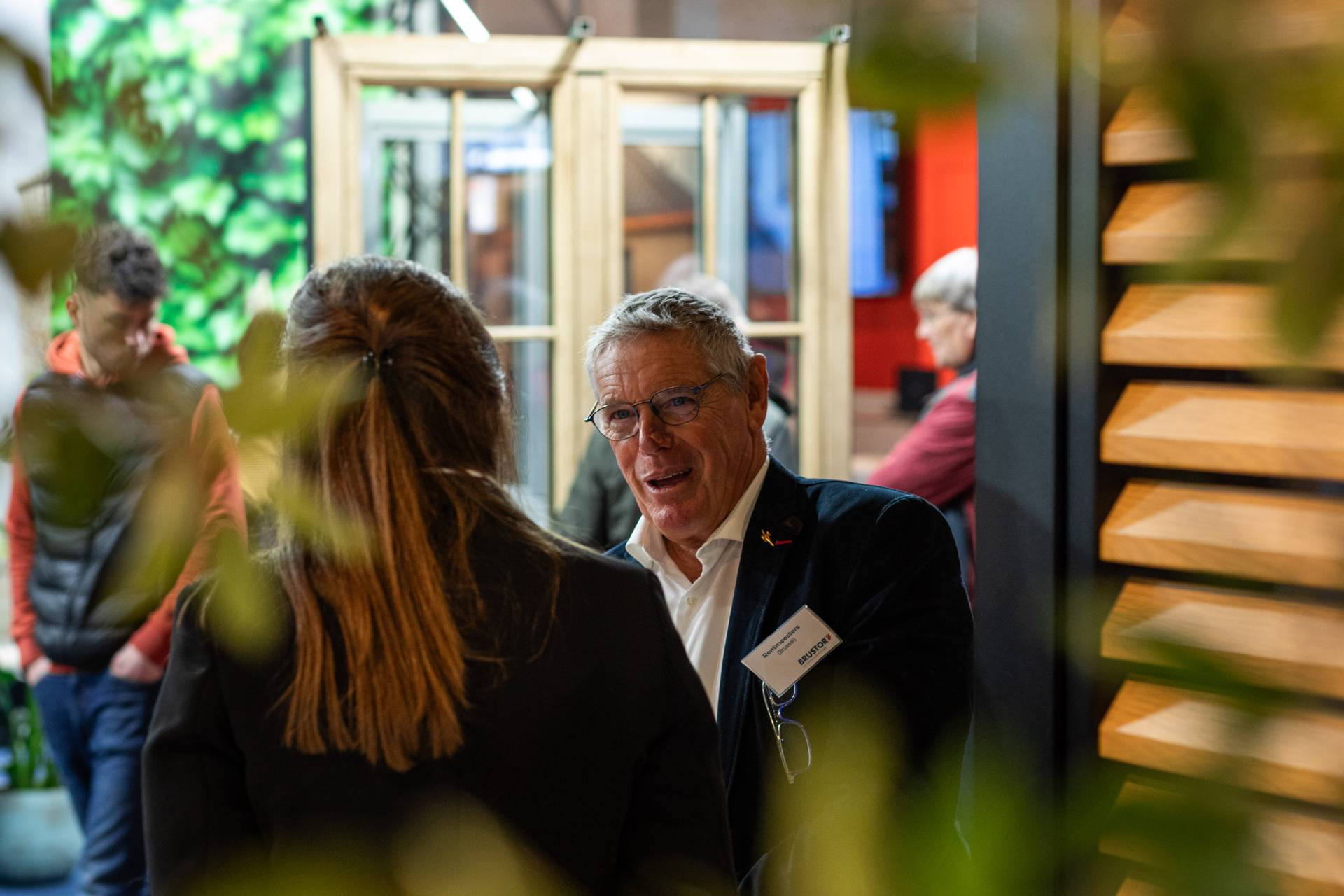 Gesprek aan de Brustor‑stand, met productpresentaties en warme standverlichting op de achtergrond.”
