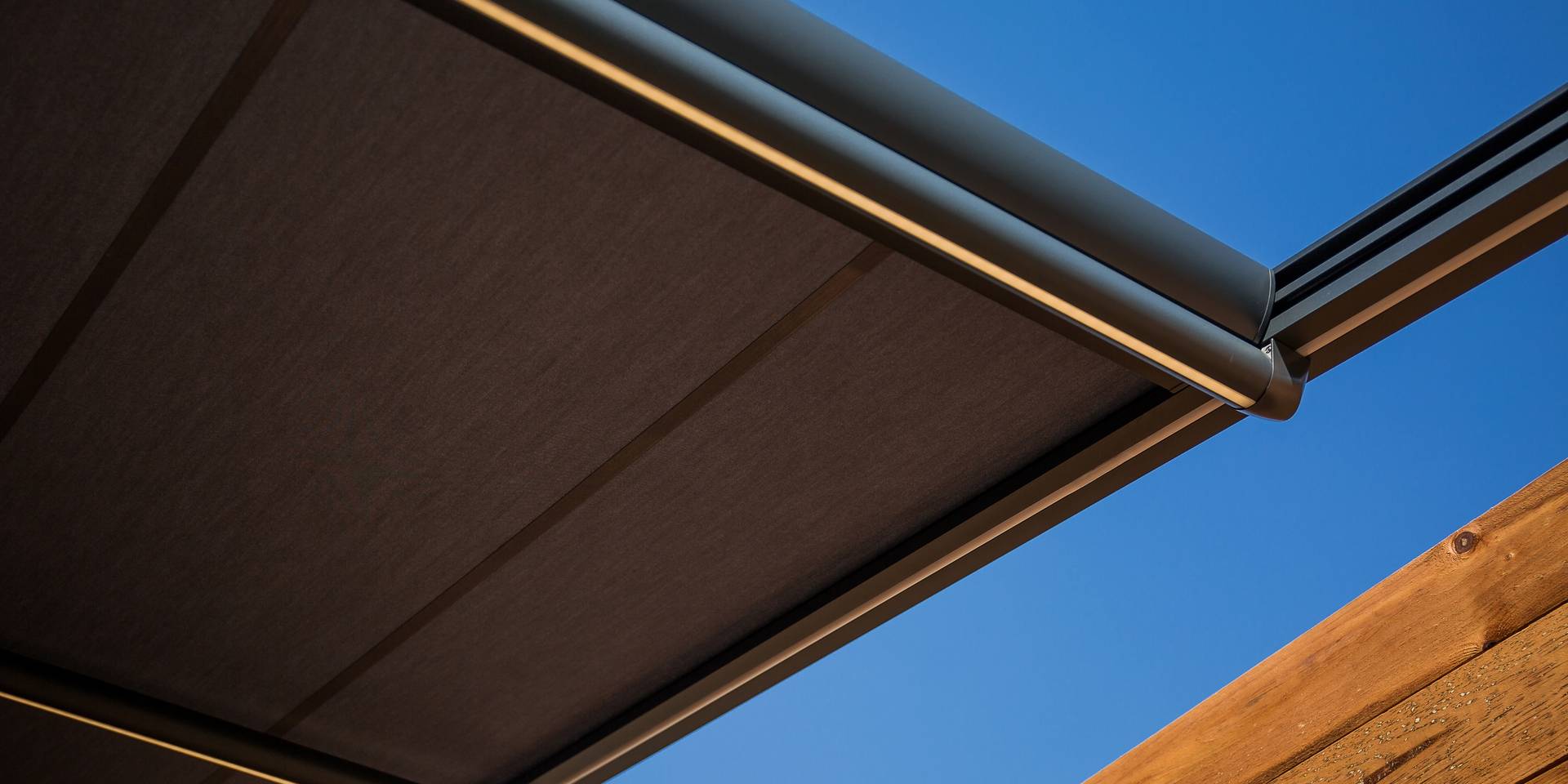 Close‑up of an aluminium awning with extended fabric and sleek cassette housing, shown against a clear blue sky.