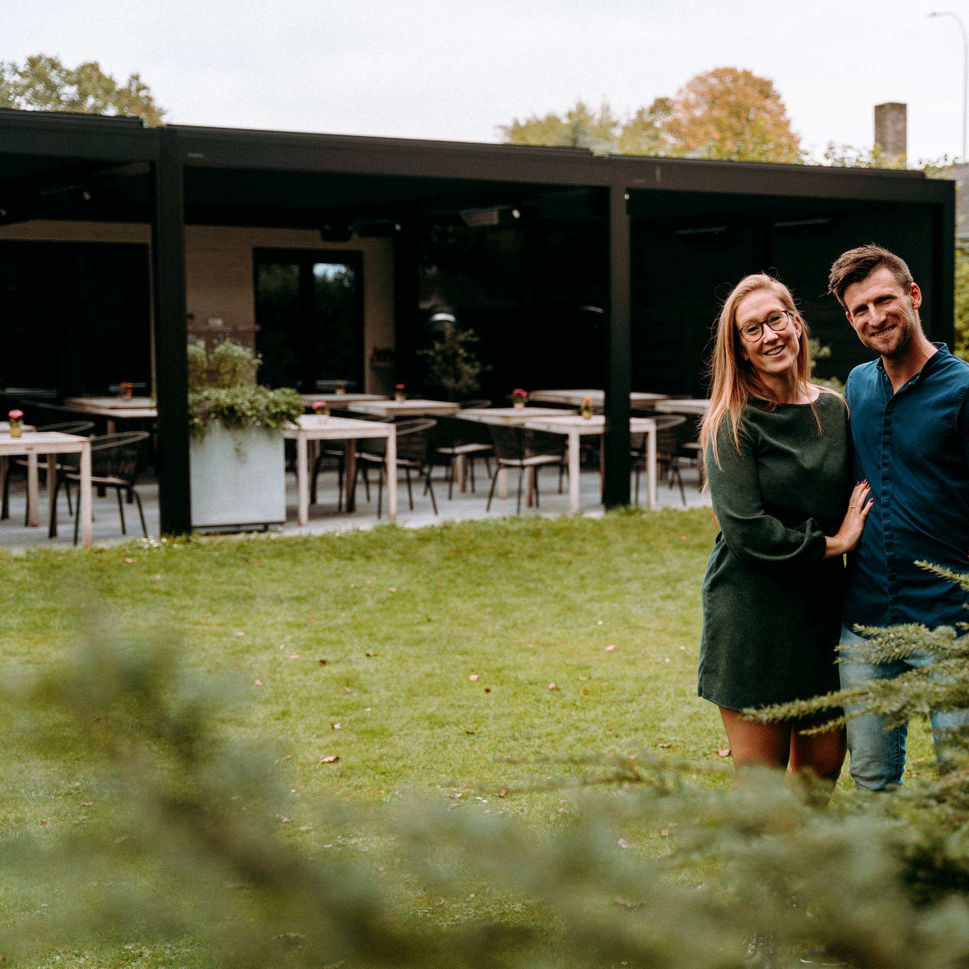 Koppel dat samen staat in een tuinomgeving met een moderne pergola en een buitendineropstelling op de achtergrond.