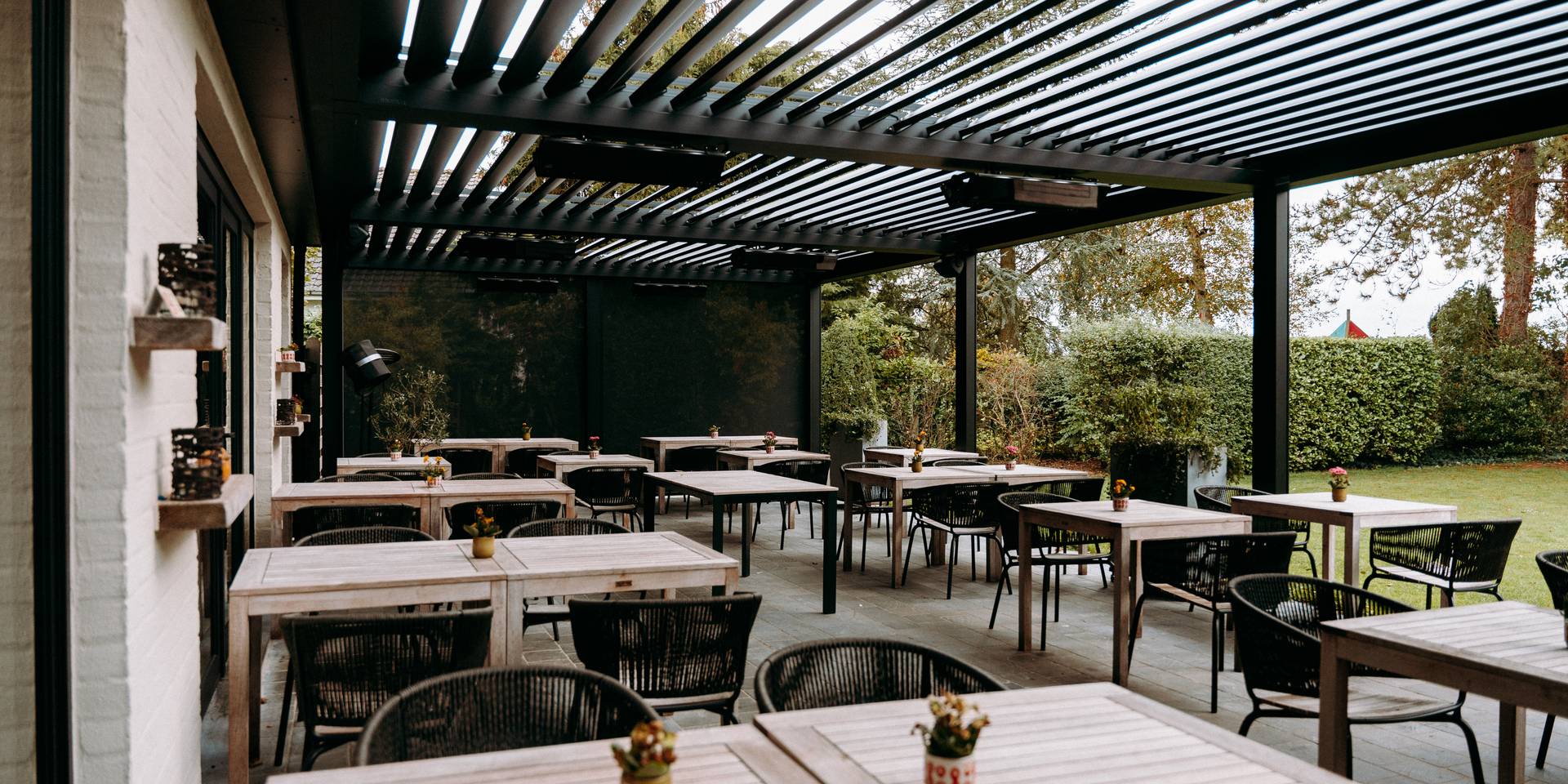 Area pranzo esterna allestita sotto una pergola moderna con lamelle regolabili e vista sul giardino.