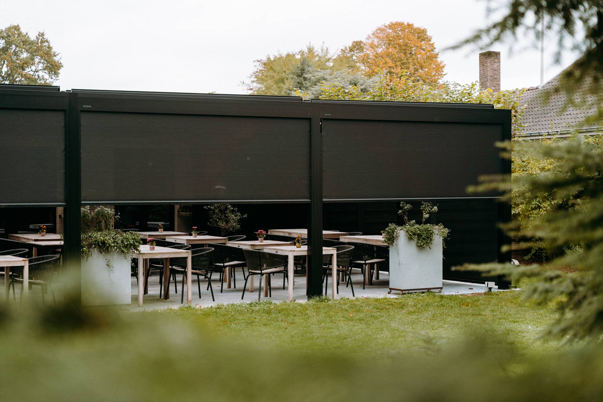 Area pranzo esterna sotto una pergola moderna con screen abbassati e vegetazione circostante.