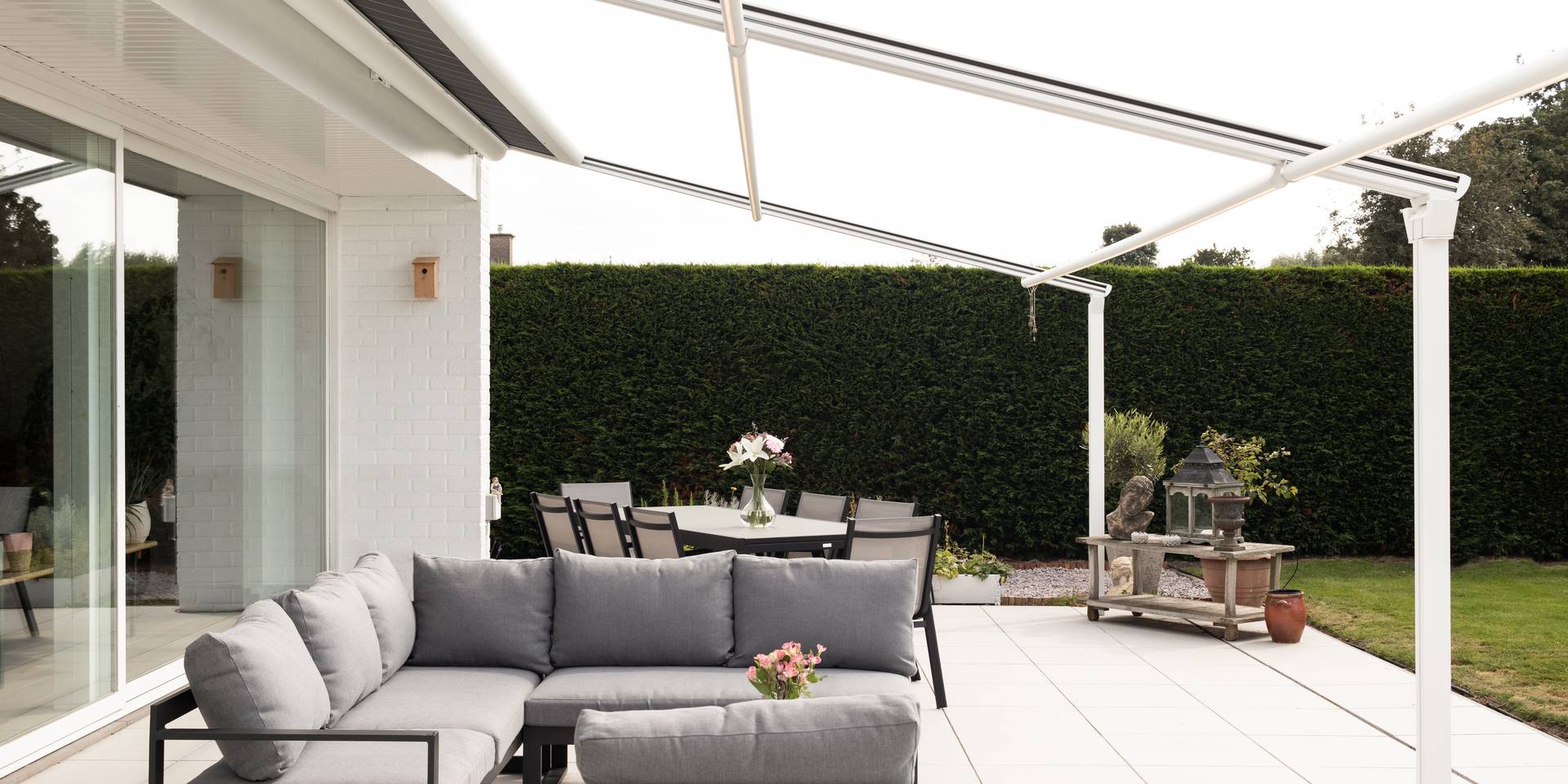 Store banne rétractable avec toile déployée couvrant une terrasse avec espace lounge et repas, attenante à une maison blanche.