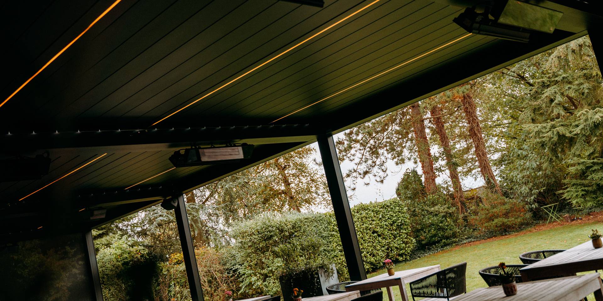 Vista di una pergola moderna con illuminazione integrata e riscaldamento esterno affacciata sul giardino.