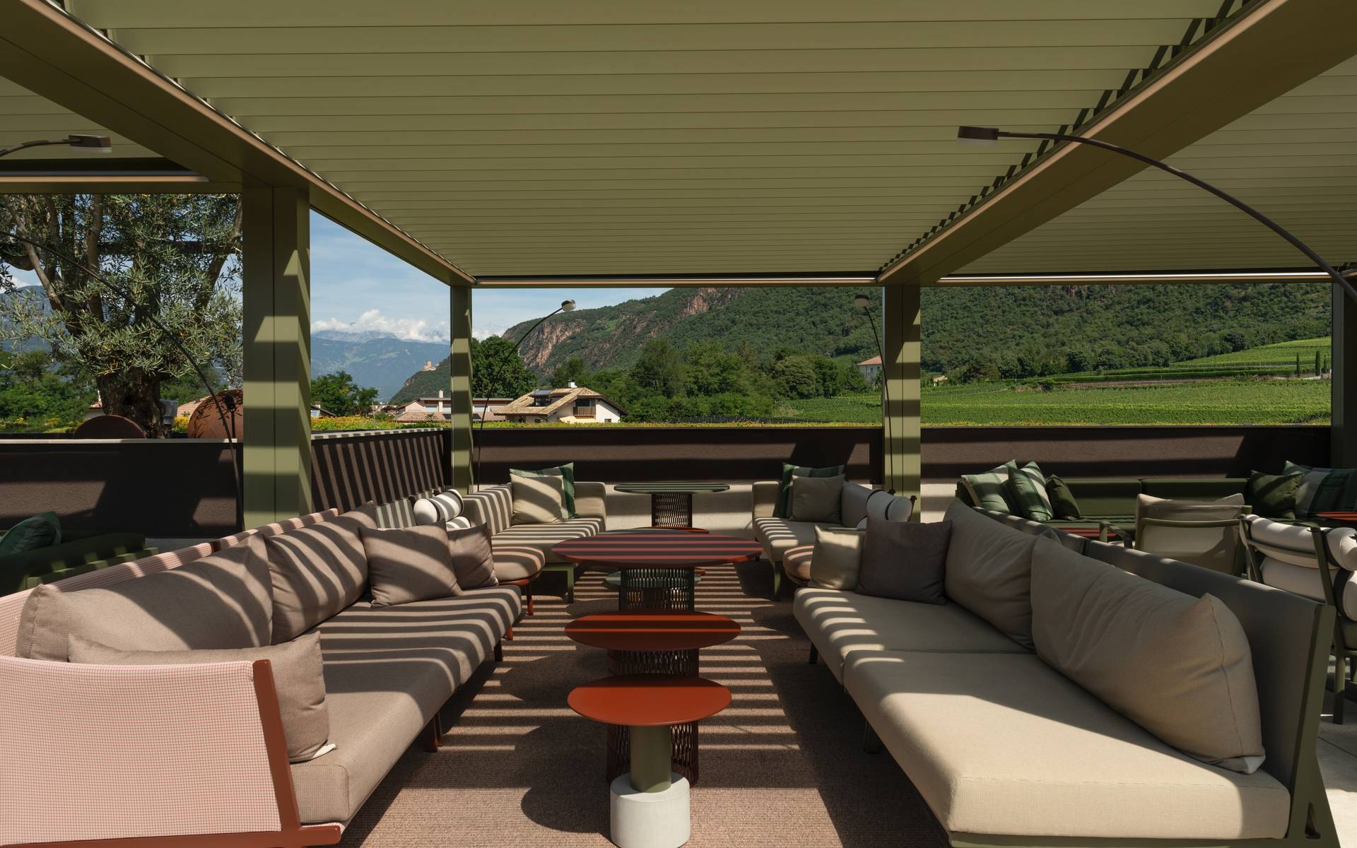 Area lounge esterna arredata sotto una pergola moderna con vista su montagne e vigneti.