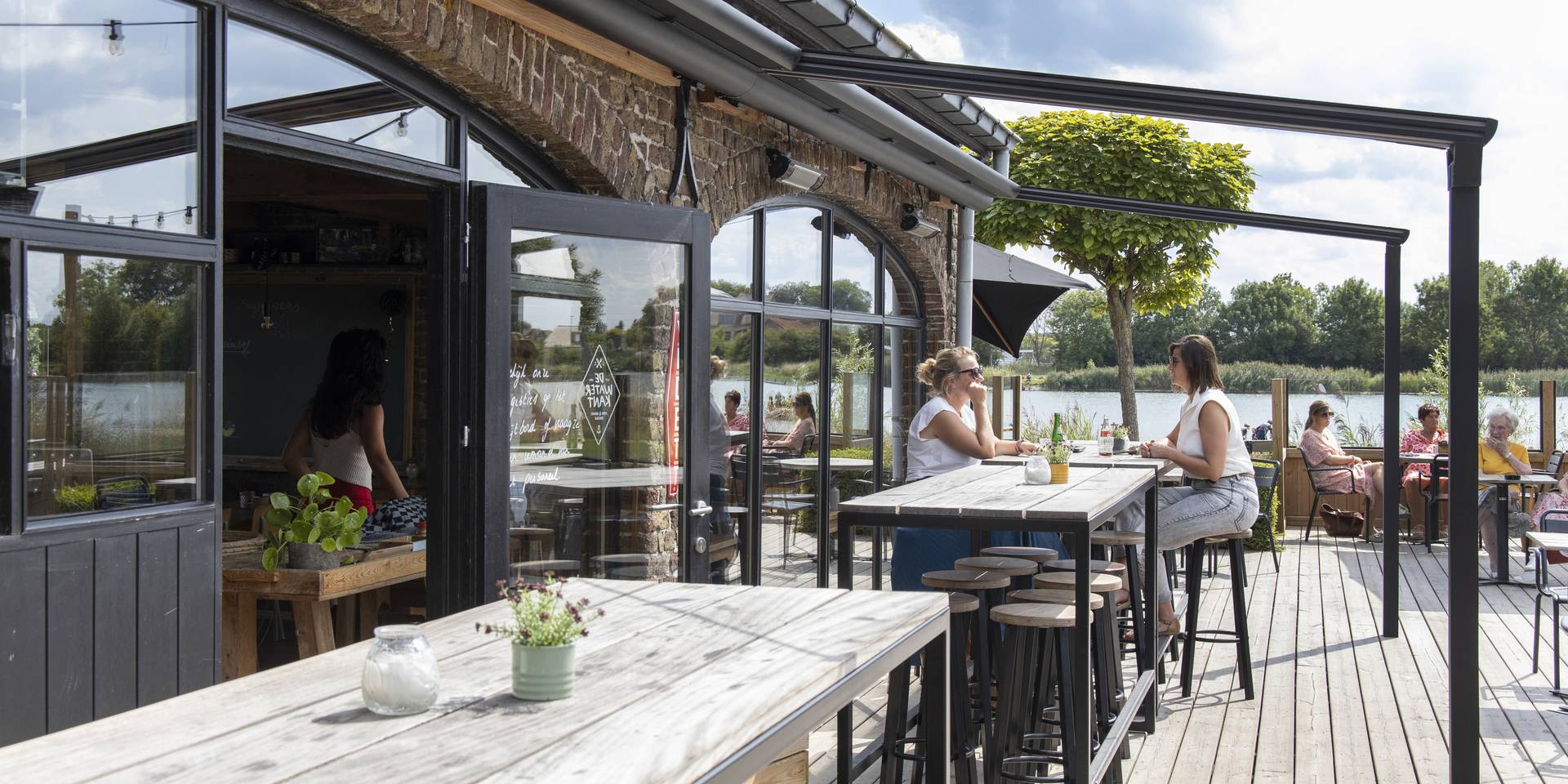 Außenterrasse eines Gastronomiebetriebs mit einer Brustor‑Pergola aus Aluminium und ausfahrbarem Stoffdach, die Schatten und Komfort in einer Lage am See bietet.