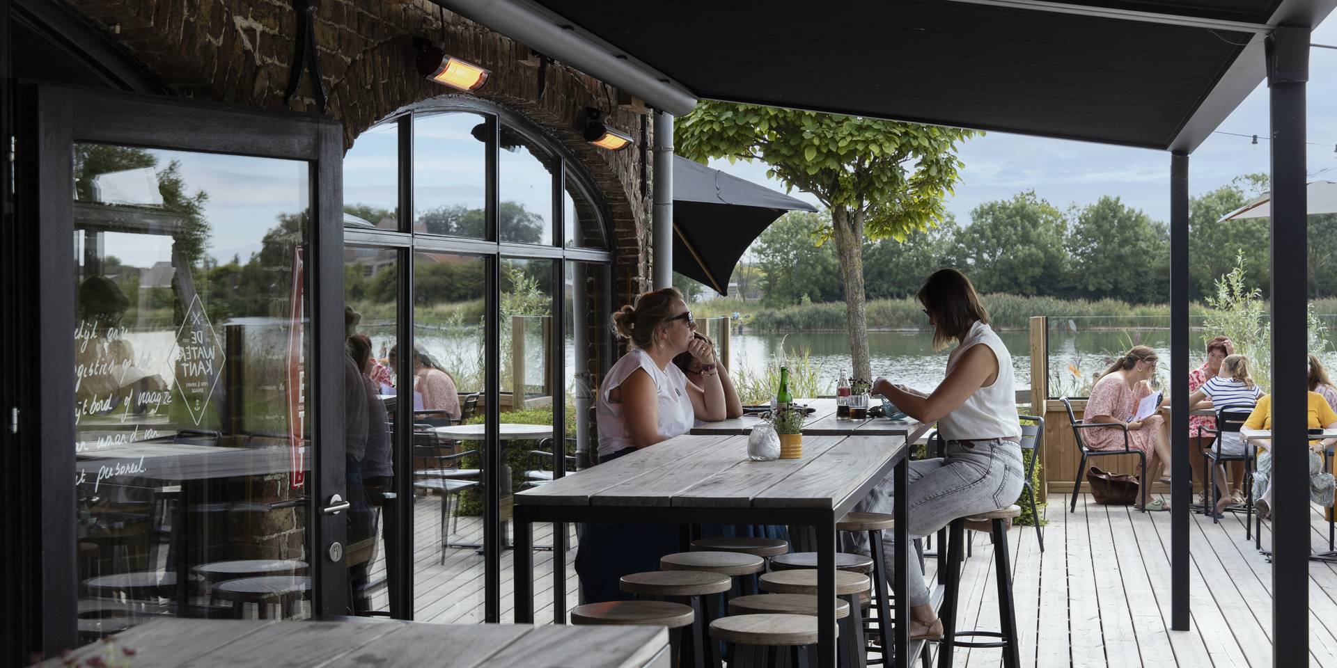 Außenterrasse eines Gastronomiebetriebs mit einer Brustor‑Pergola aus Aluminium und ausfahrbarem Stoffdach, die Schatten und Komfort in einer Lage am See bietet.