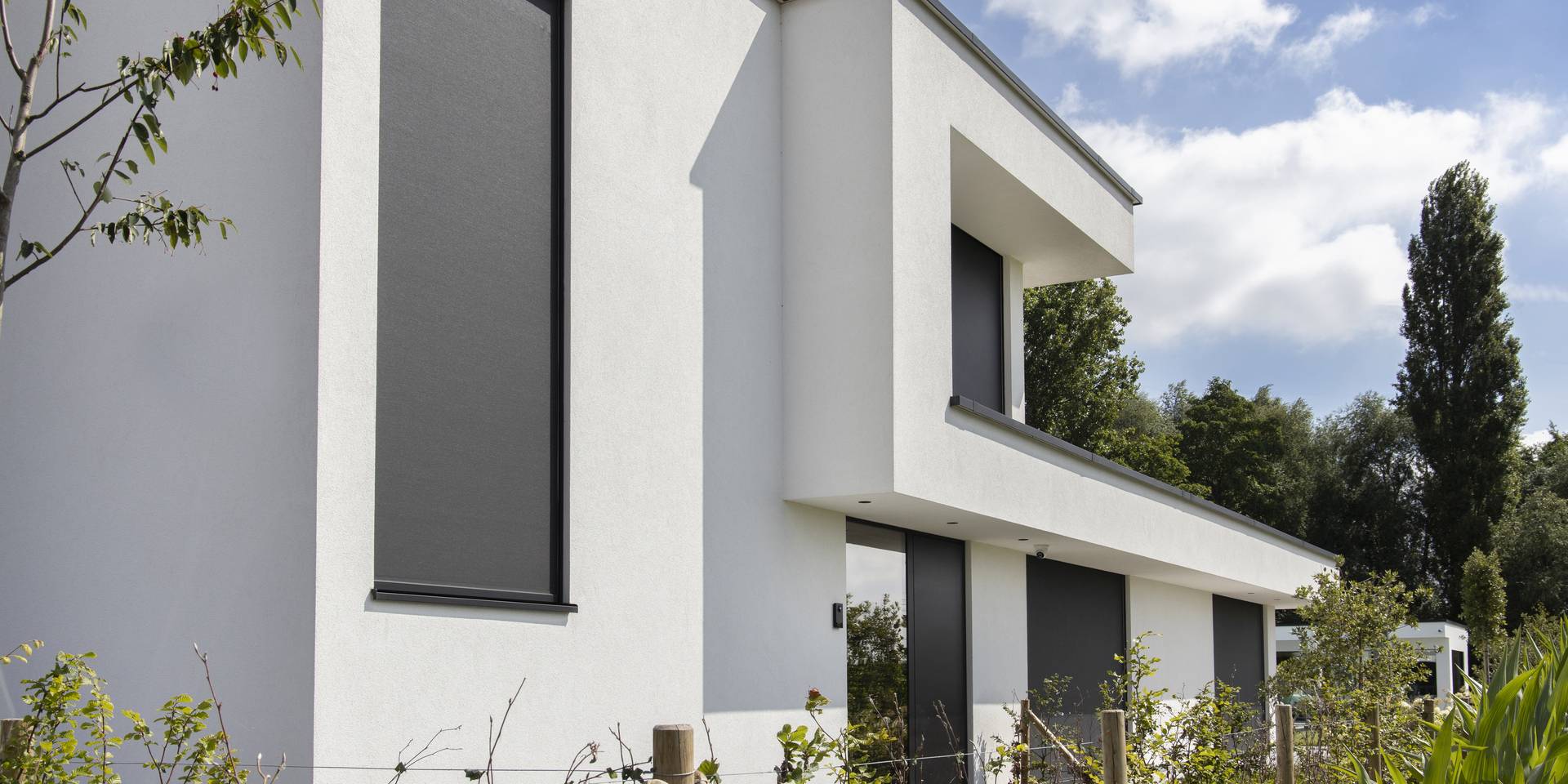 Modern house with aluminium ZIP‑screens installed on tall windows, providing exterior sun protection in a landscaped garden setting.