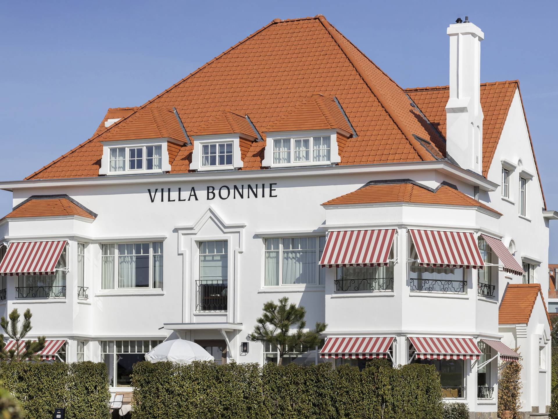 Gelenkarmmarkisen mit rot‑weiß gestreiftem Tuch an der Fassade einer klassischen Villa