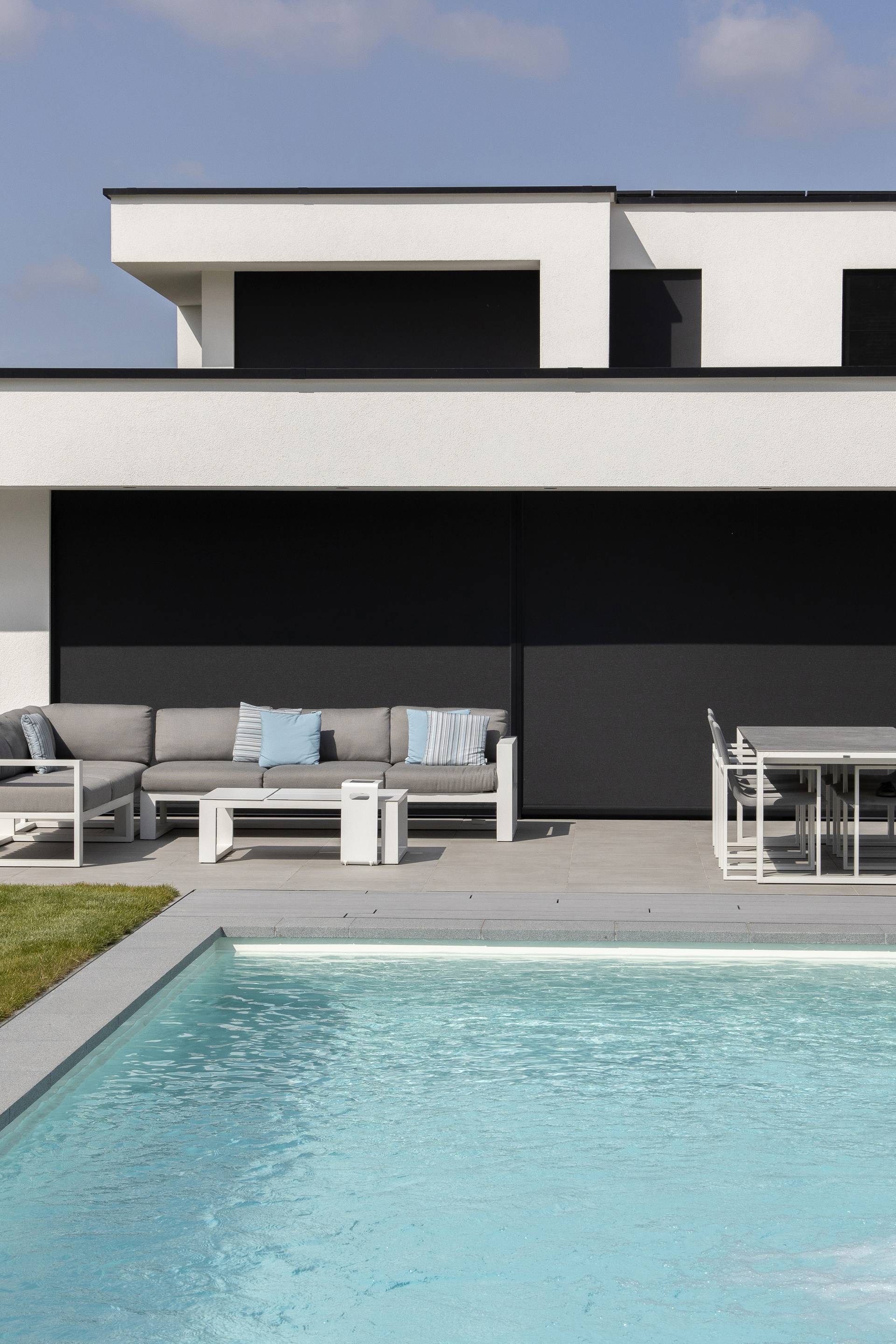 Modern buitenterras met geïntegreerde Brustor ZIP‑screens in een strakke witte nieuwbouwwoning, met een stijlvolle loungeset en eethoek met zicht op de tuin.