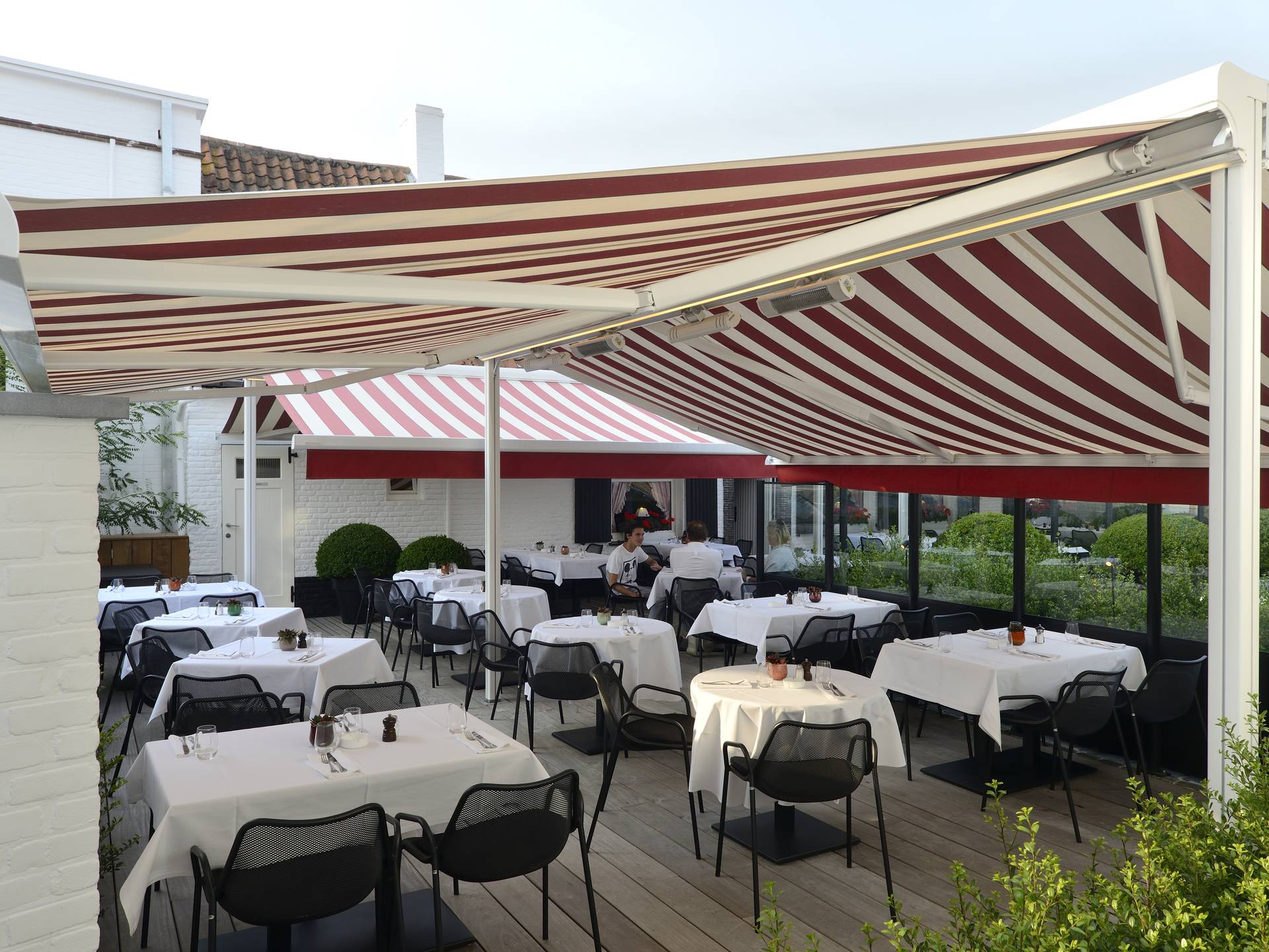 Gelenkarmmarkisen mit rot‑weiß gestreiftem Tuch über der Außen­terrasse eines Restaurants