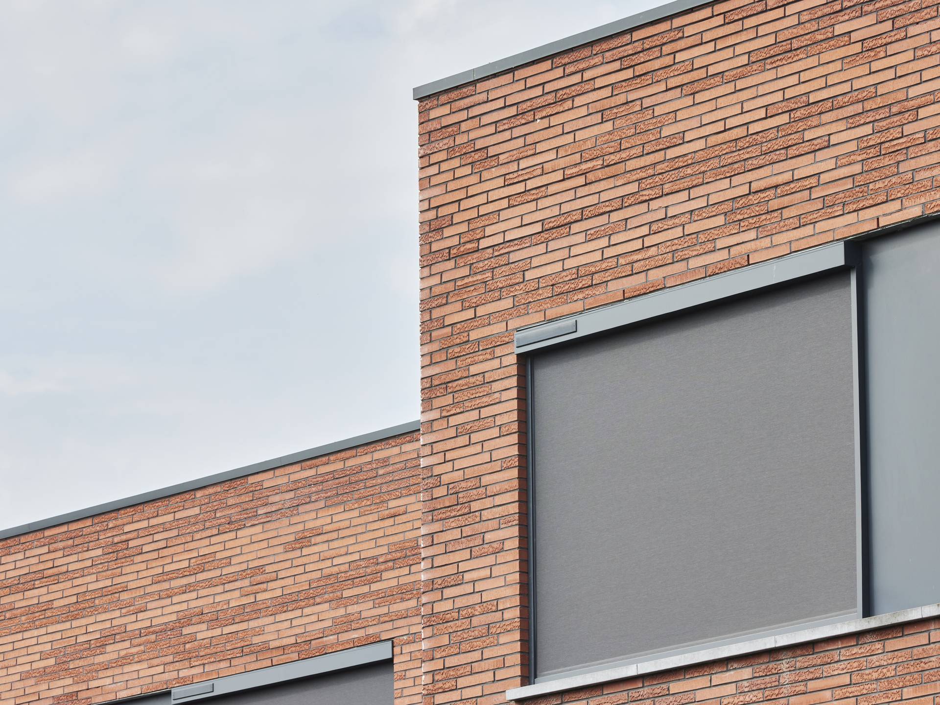 Façade moderne en briques avec store screen vertical extérieur fermé, intégré au-dessus de la fenêtre pour la protection solaire.