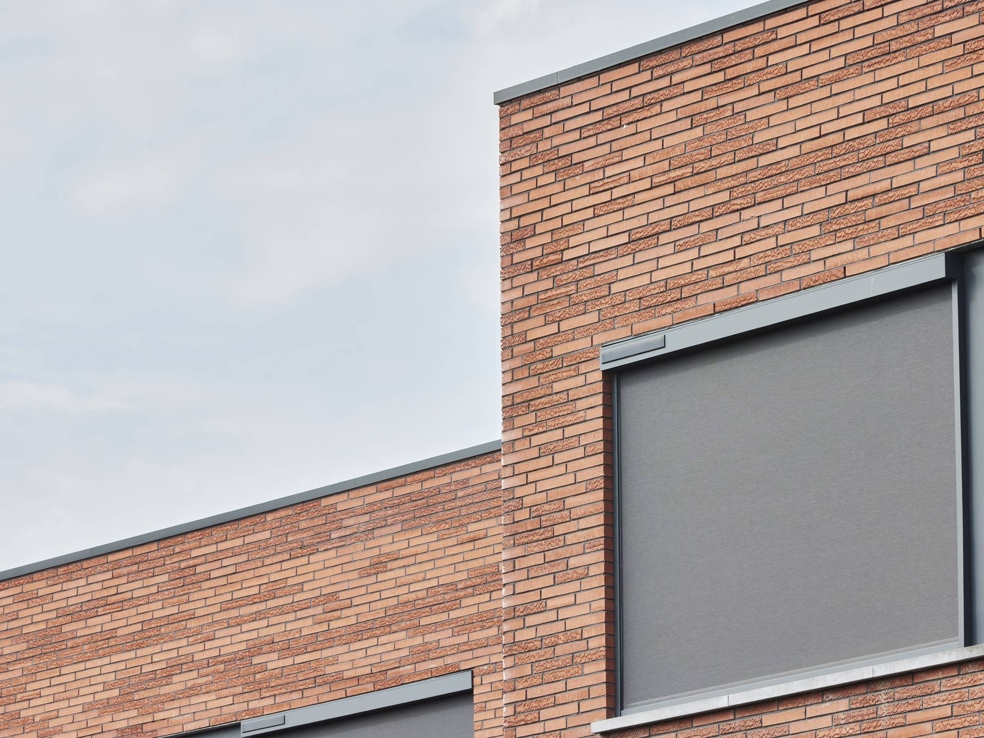 Façade moderne en briques avec store screen vertical extérieur fermé, intégré au-dessus de la fenêtre pour la protection solaire.