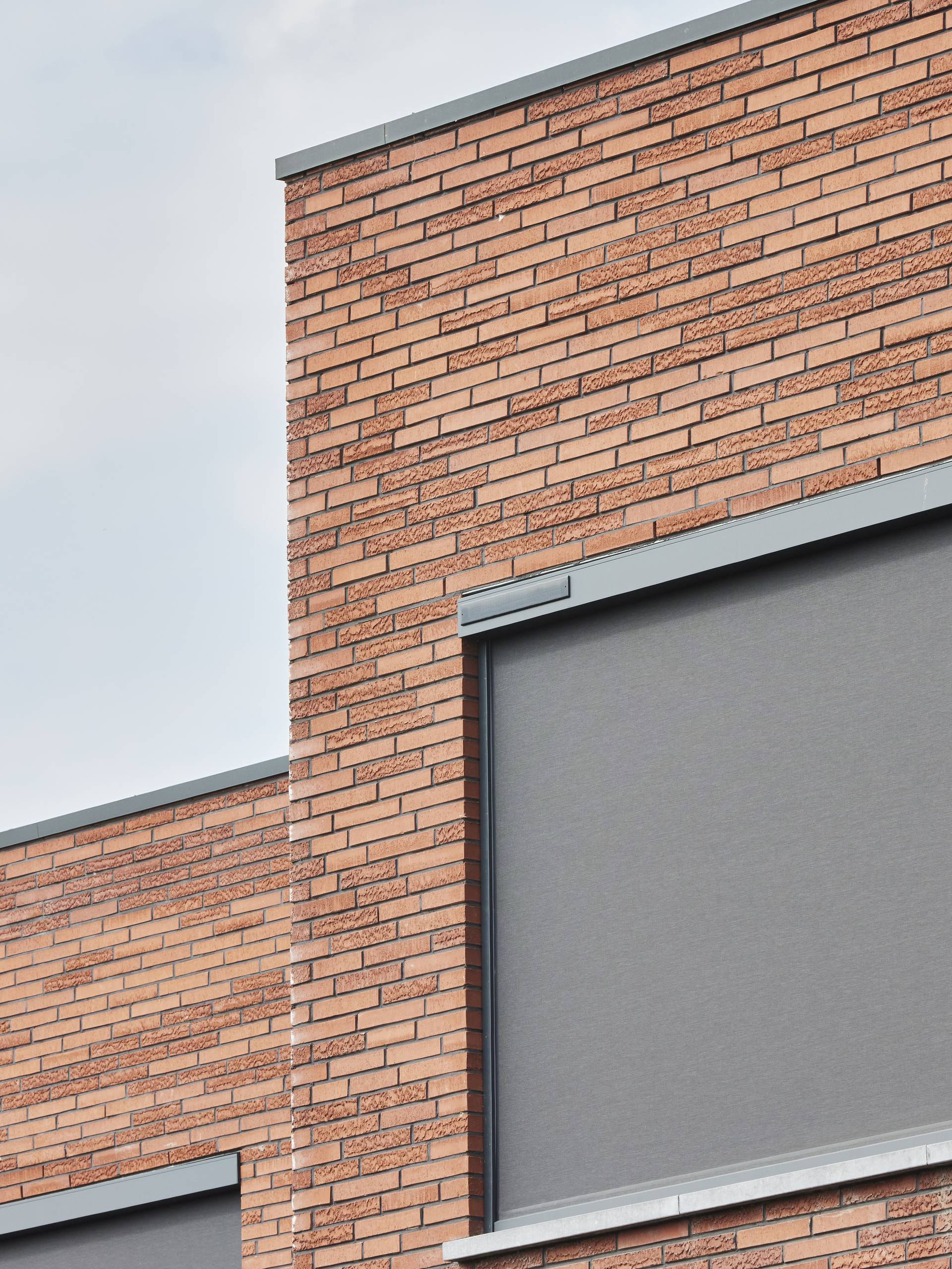 Moderne Backsteinfassade mit geschlossenem außenliegendem Vertikalscreen, oberhalb des Fensters integriert als Sonnenschutz.