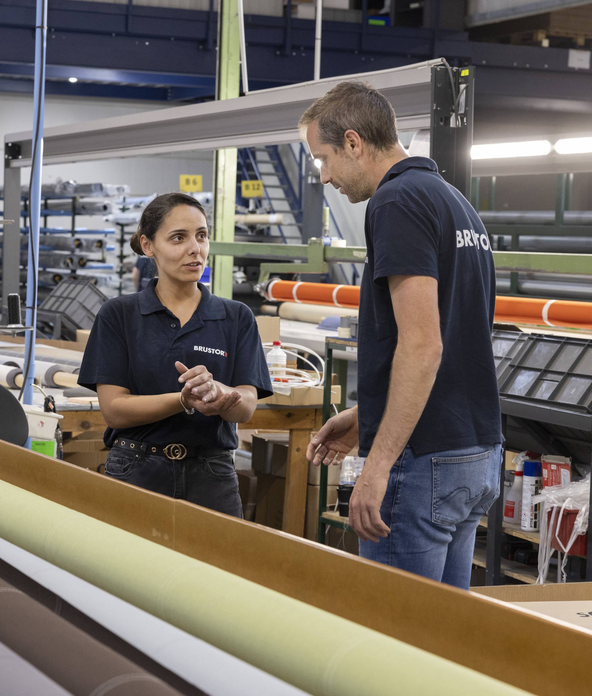Twee Brustor‑medewerkers die werkafspraken bespreken naast productieapparatuur in de productiehal.