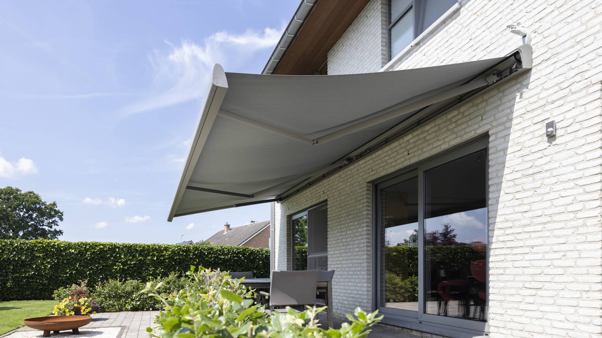 Store banne rétractable en aluminium déployé au‑dessus de la terrasse d’une maison moderne en briques, ombrageant l’espace repas extérieur.