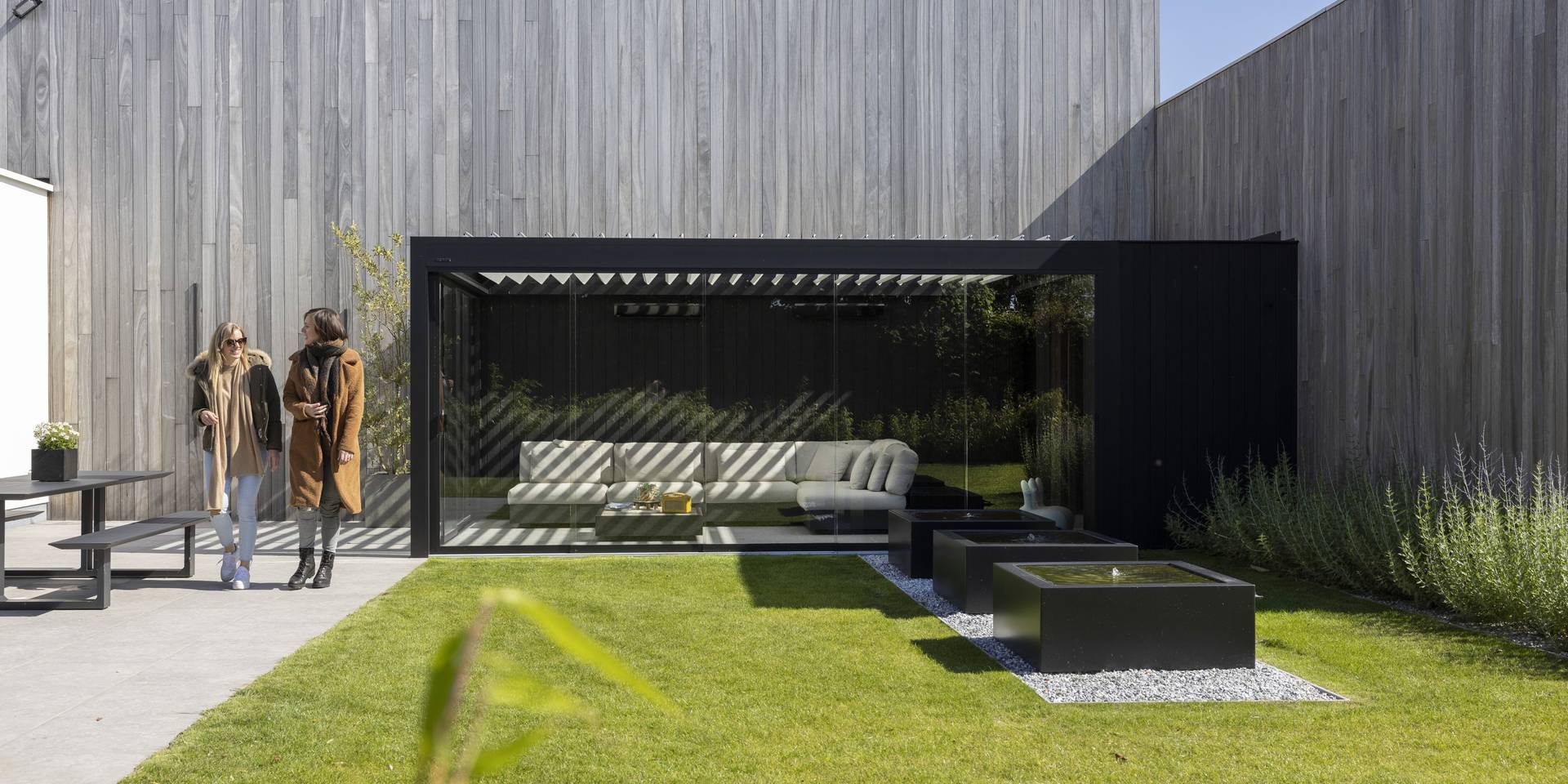 Modern home with large glass terrace cover and garden, two people walking on the patio in front of the house