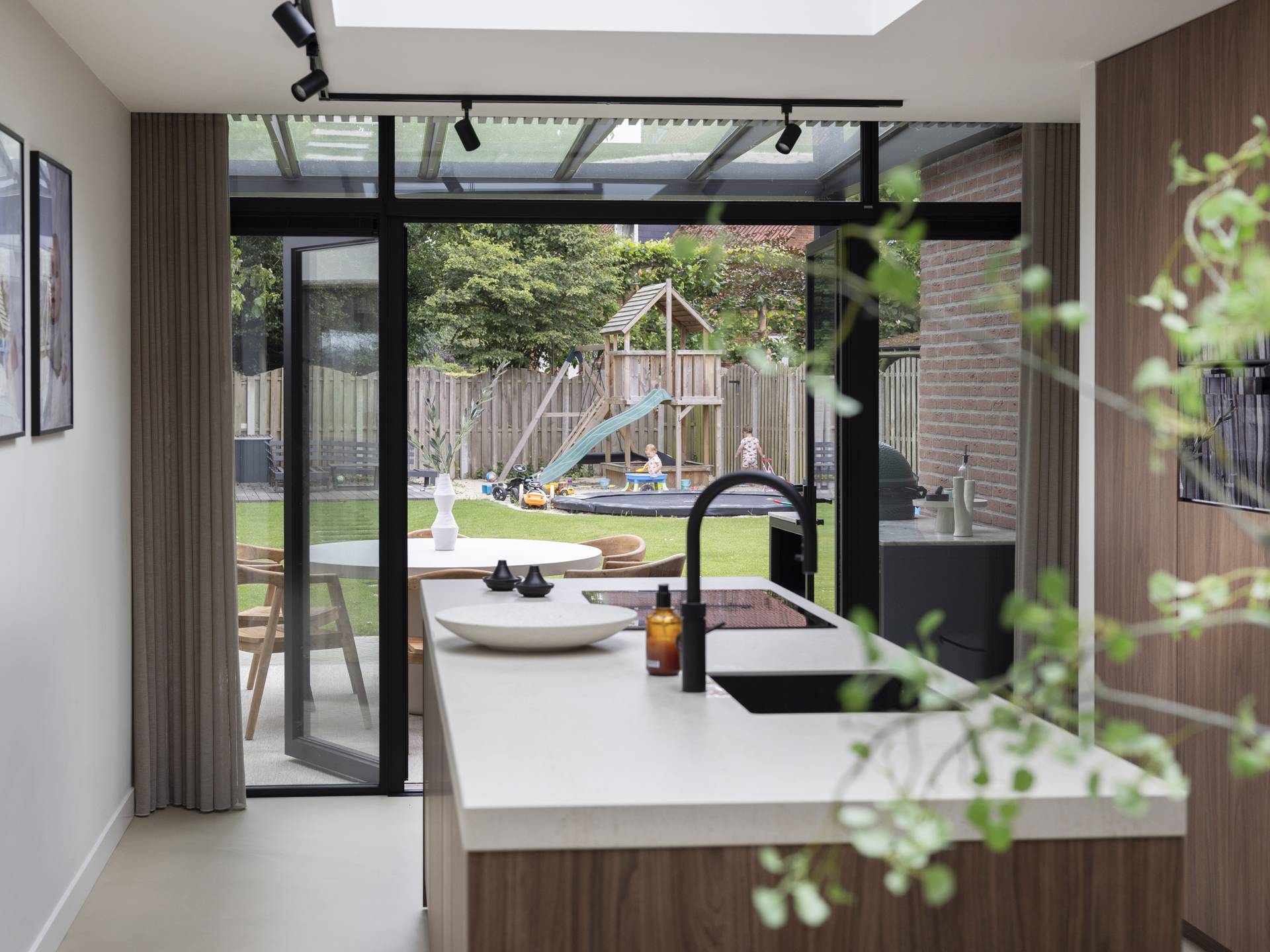 Vue intérieure sur une pergola B800 en aluminium avec toit en verre reliant la cuisine à un espace repas extérieur lumineux avec vue sur le jardin
