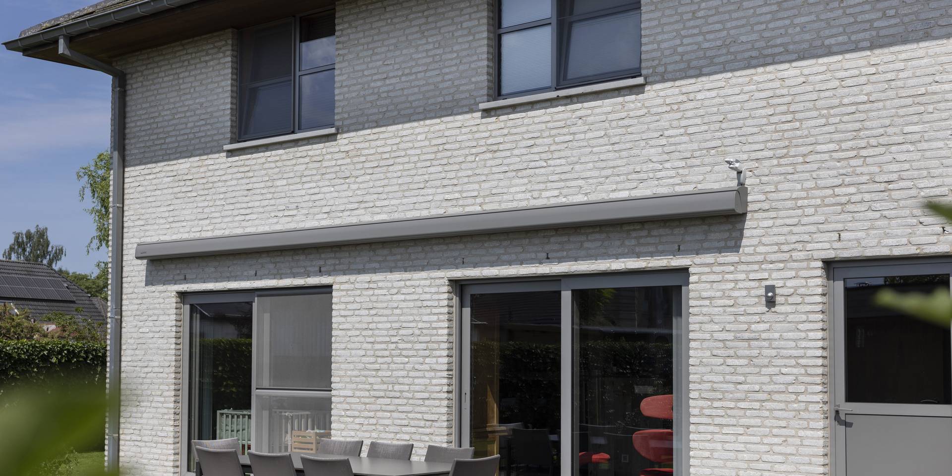 Store banne à cassette fermée installé sur la façade d’une maison moderne en briques, au‑dessus d’une terrasse avec espace repas extérieur.
