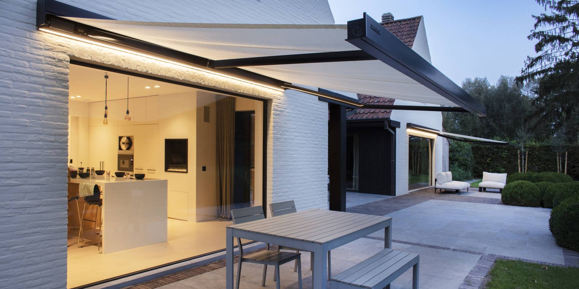 Aluminium awnings with integrated LED lighting extending over a modern terrace, providing shade beside a contemporary white house.