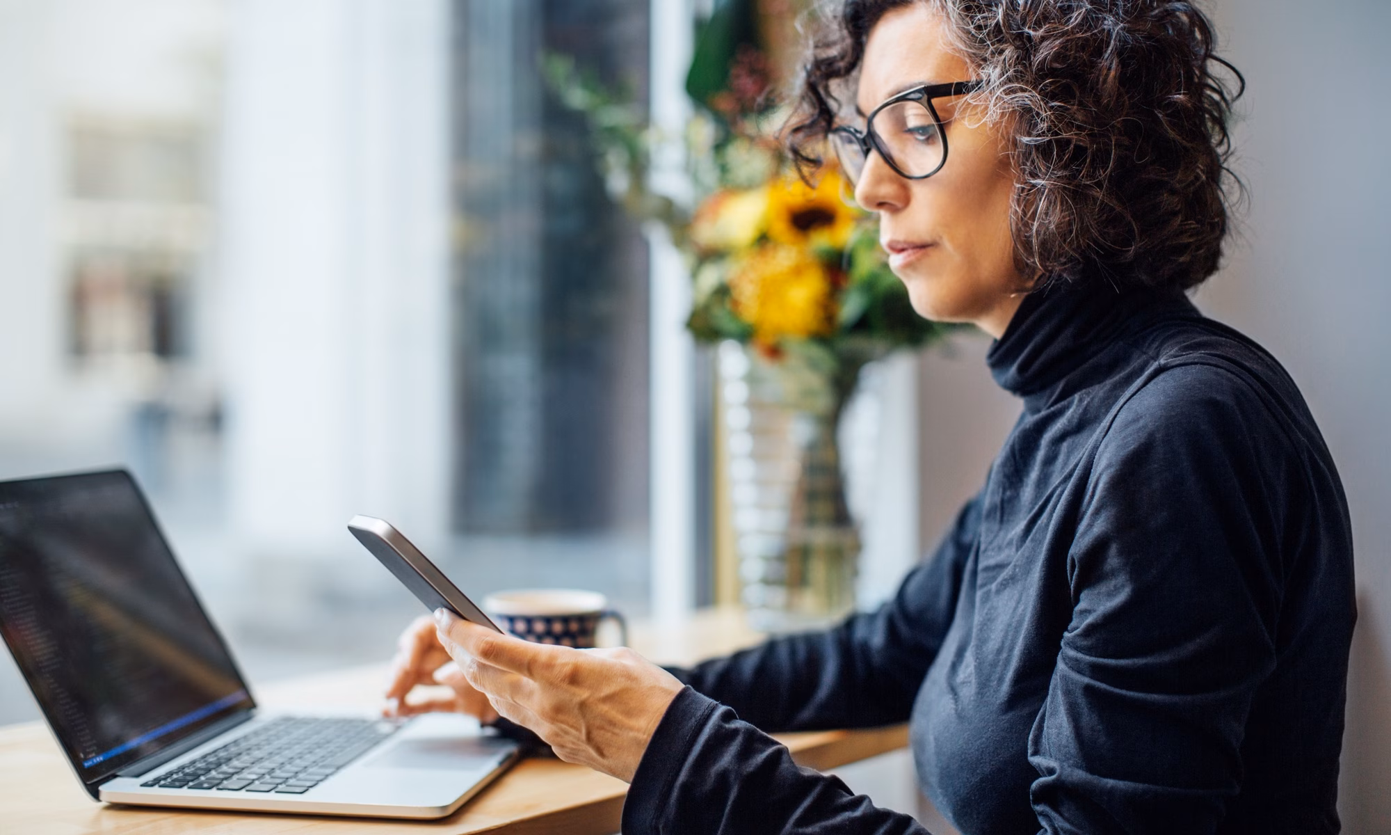 Frau mit Laptop und Handy, Blumen im Hintergrund