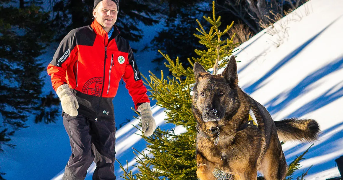 Ein Mitarbeirter der Österreichischen Bergrettung und ein Schäferhund im Schnee