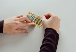 Jemand rubbelt mit einer Münze ein Rubbellos auf