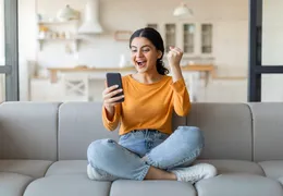 eine junge Frau freut sich über einen Gewinn und sitzt auf der Couch