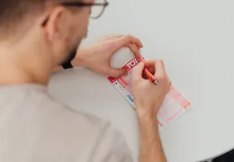 ein junger Mann füllt einen Toto Wettschein aus