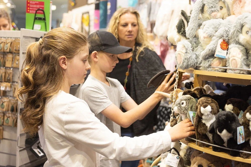 Children and a woman browsing animals toys in the wildlife centre shop, plush toys on a shelf.