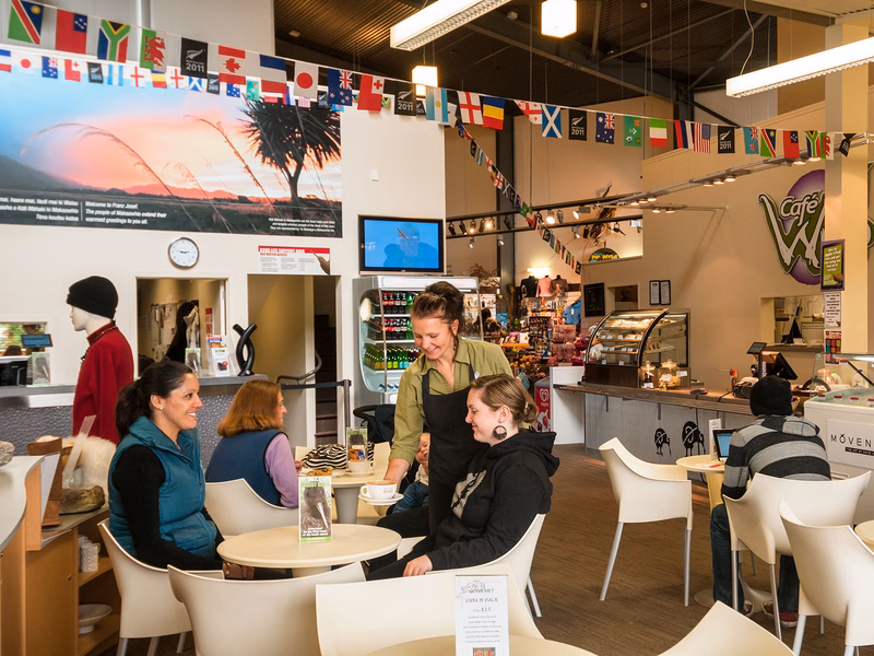 A cozy café with patrons seated at tables, a server attending to them, and flags hanging from the ceiling. The atmosphere is warm and inviting.