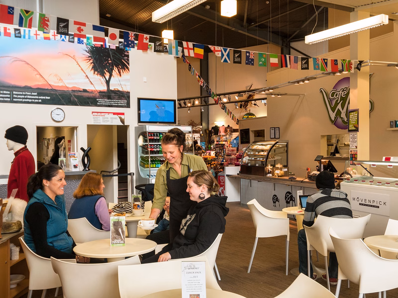 A cozy café with patrons seated at tables, a server attending to them, and flags hanging from the ceiling. The atmosphere is warm and inviting.