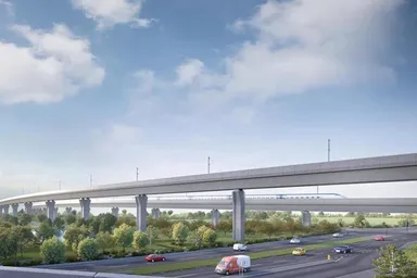 Concrete elevated rail viaduct with a high-speed train passing above a multi-lane highway, cars below and green fields under a blue sky.